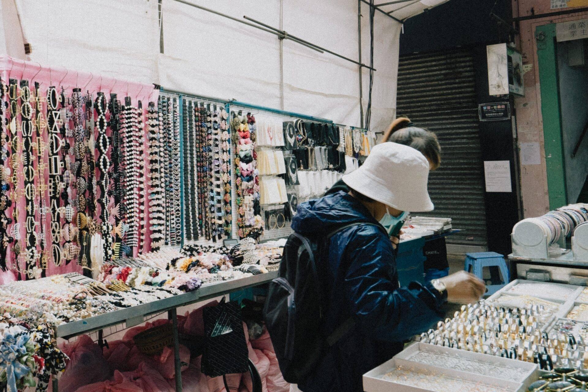 Une vendeuse de bijoux et accessoires dans un marché couvert asiatique, exposant colliers et bracelets colorés