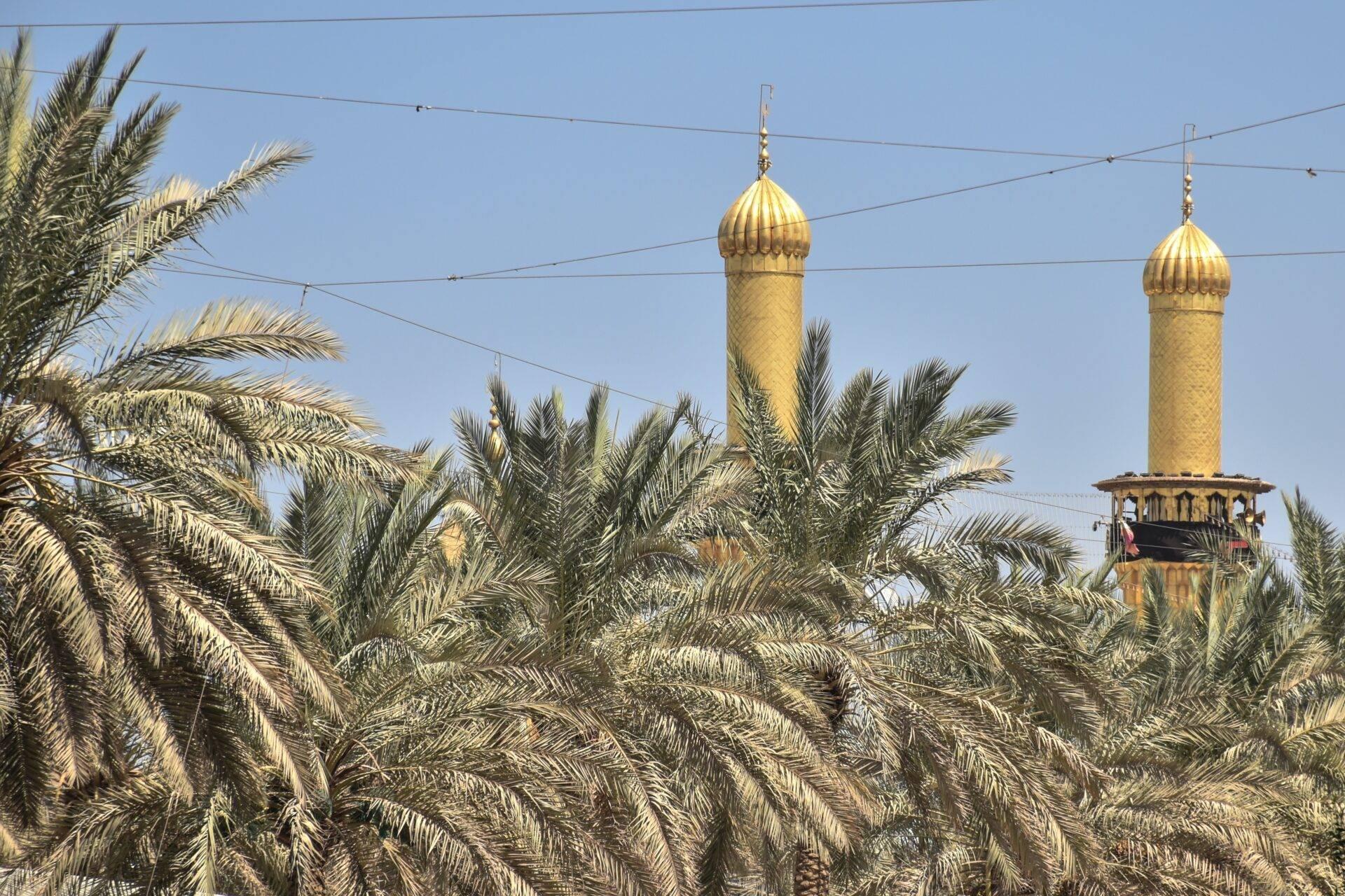 Deux minarets dorés avec dômes bulbeux émergent parmi des palmiers dattiers sous un ciel bleu