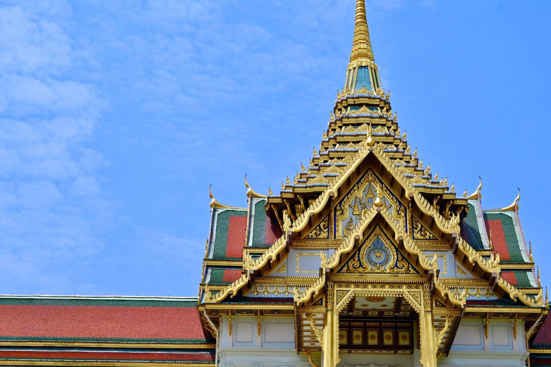 Un temple bouddhiste thaïlandais aux toits dorés ornés, aux tuiles colorées et à l’architecture traditionnelle sous un ciel bleu