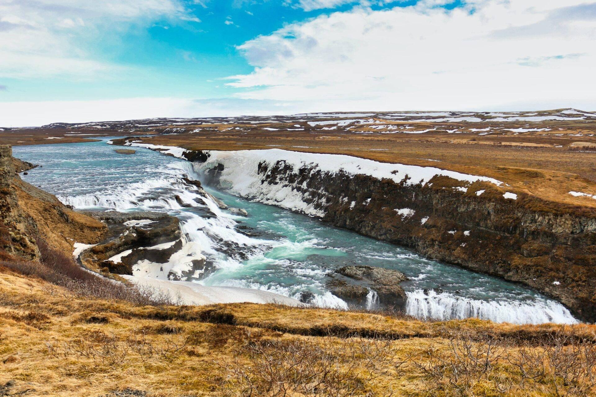 Un fiume glaciale turchese serpeggia tra scogliere innevate in un paesaggio islandese di tundra desertica