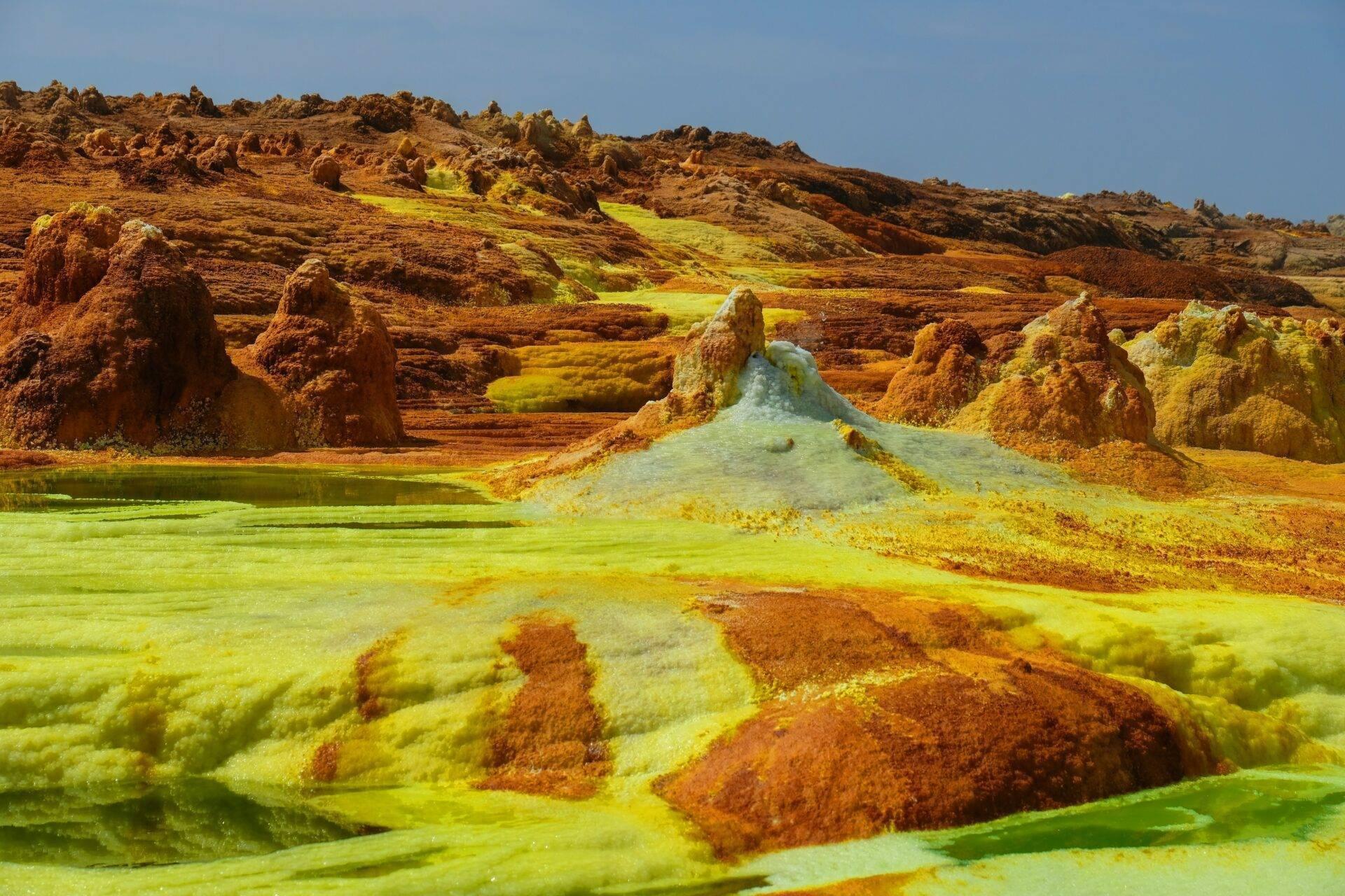 Geothermische Landschaft mit schwefelgelb gefärbten heißen Quellen und rötlich-ockerfarbenen Felsen