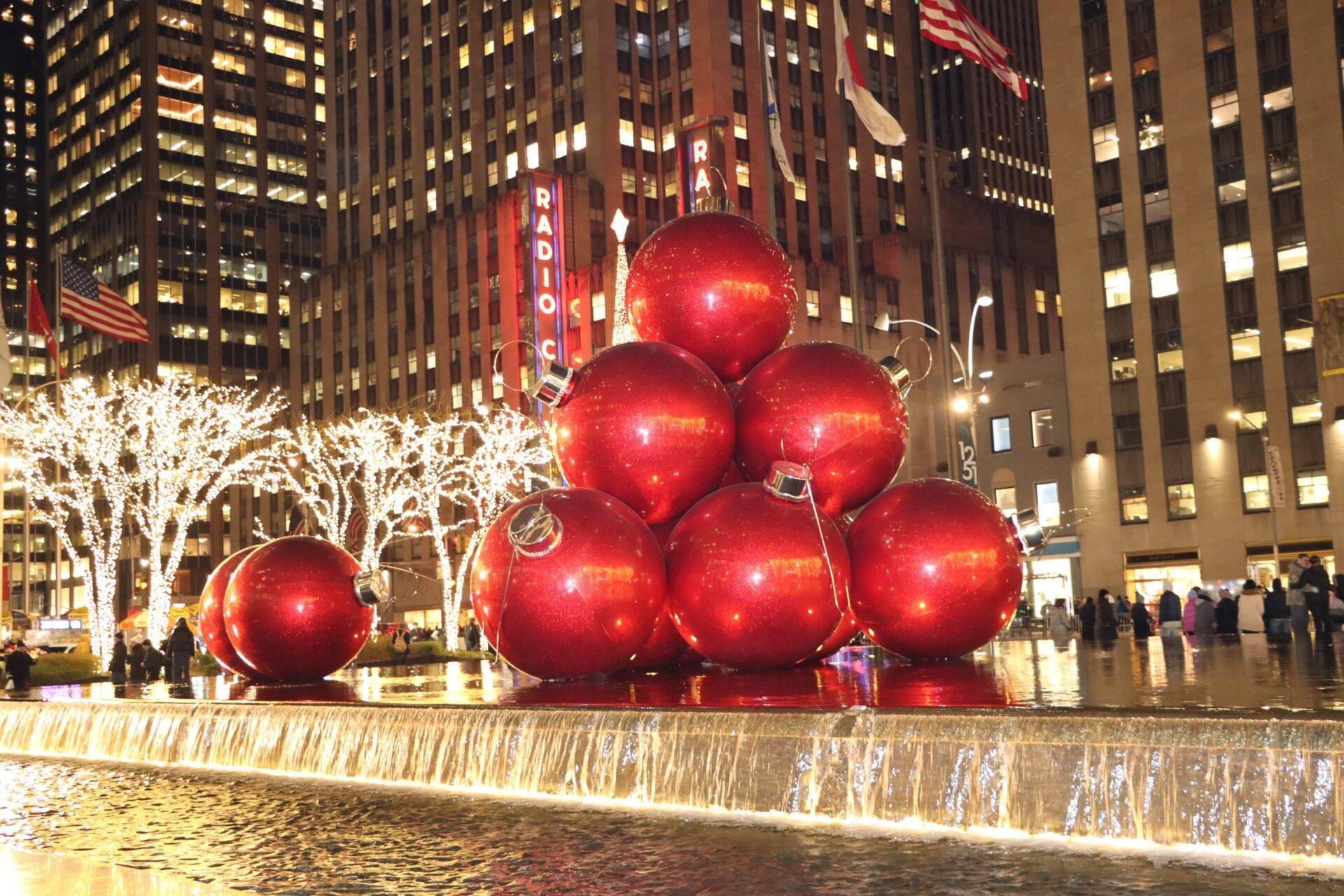 Gigantesques boules rouges de Noël illuminées dans une place urbaine entourée de gratte-ciel et de décorations festives