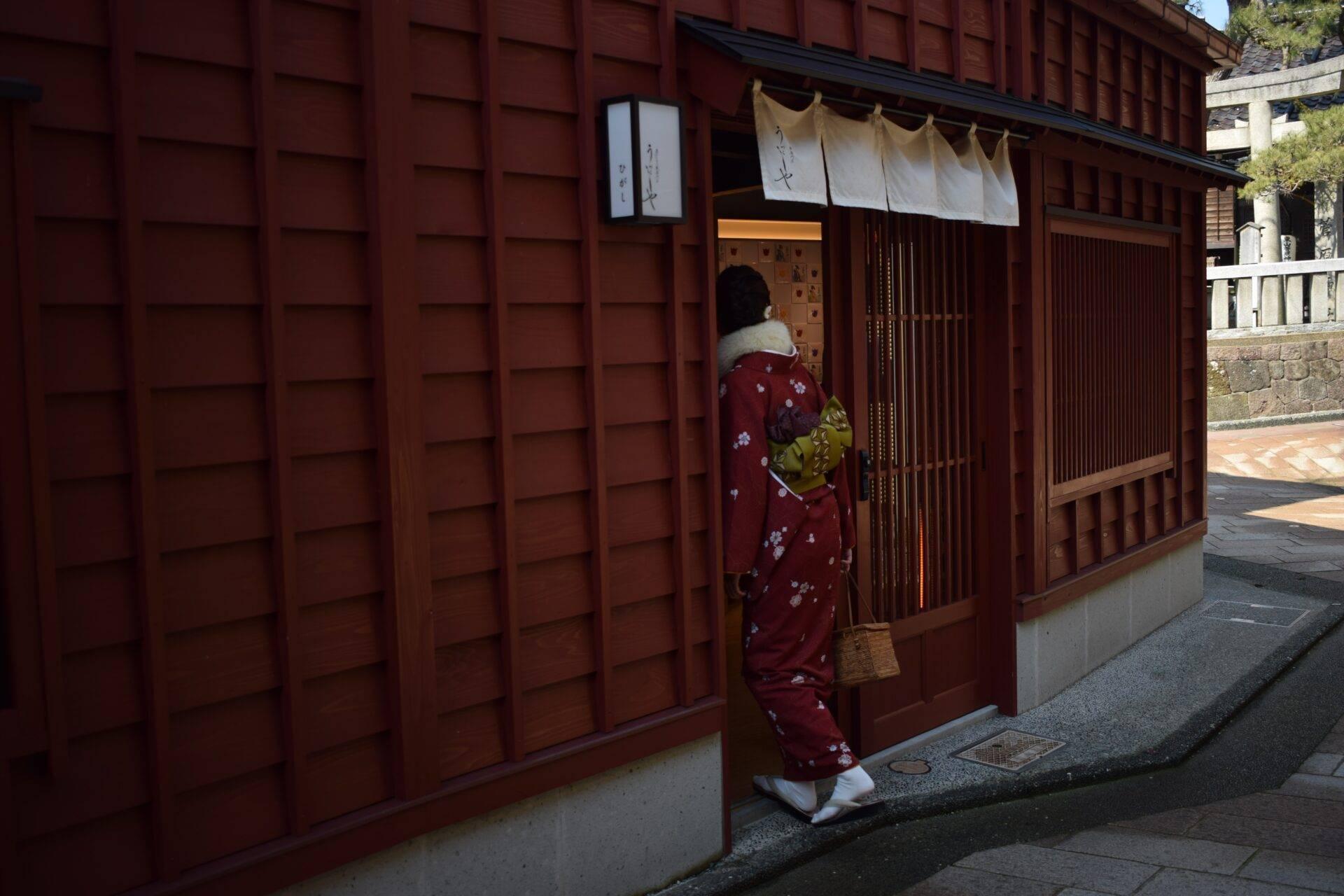 Une femme en kimono rouge entre dans un établissement traditionnel japonais aux murs et portes en bois foncé