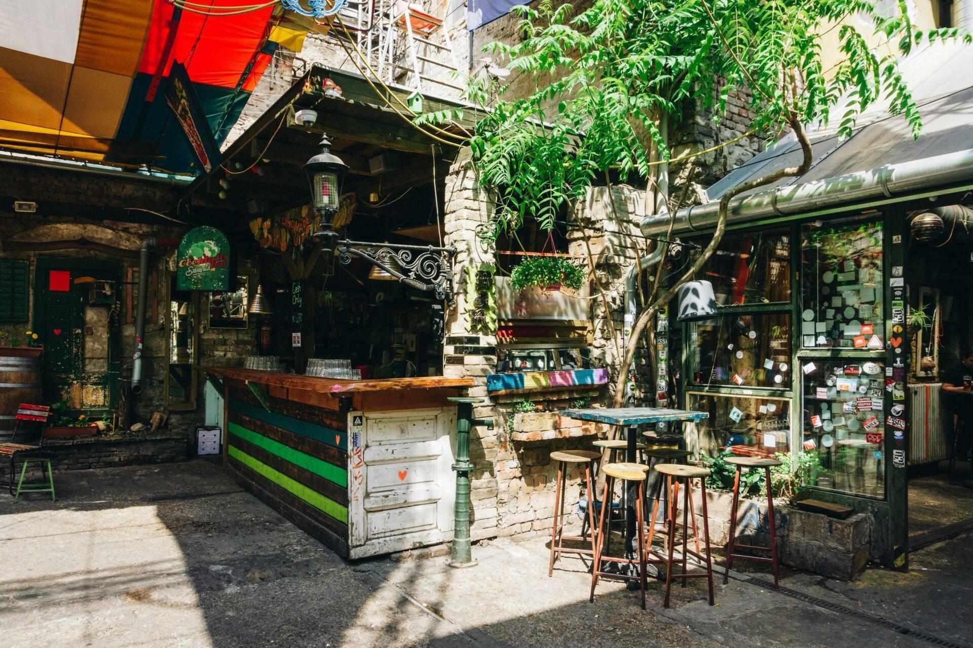 Un cortile bohémien con bar colorato, rampicanti e mobili vintage in un’atmosfera urbana alternativa