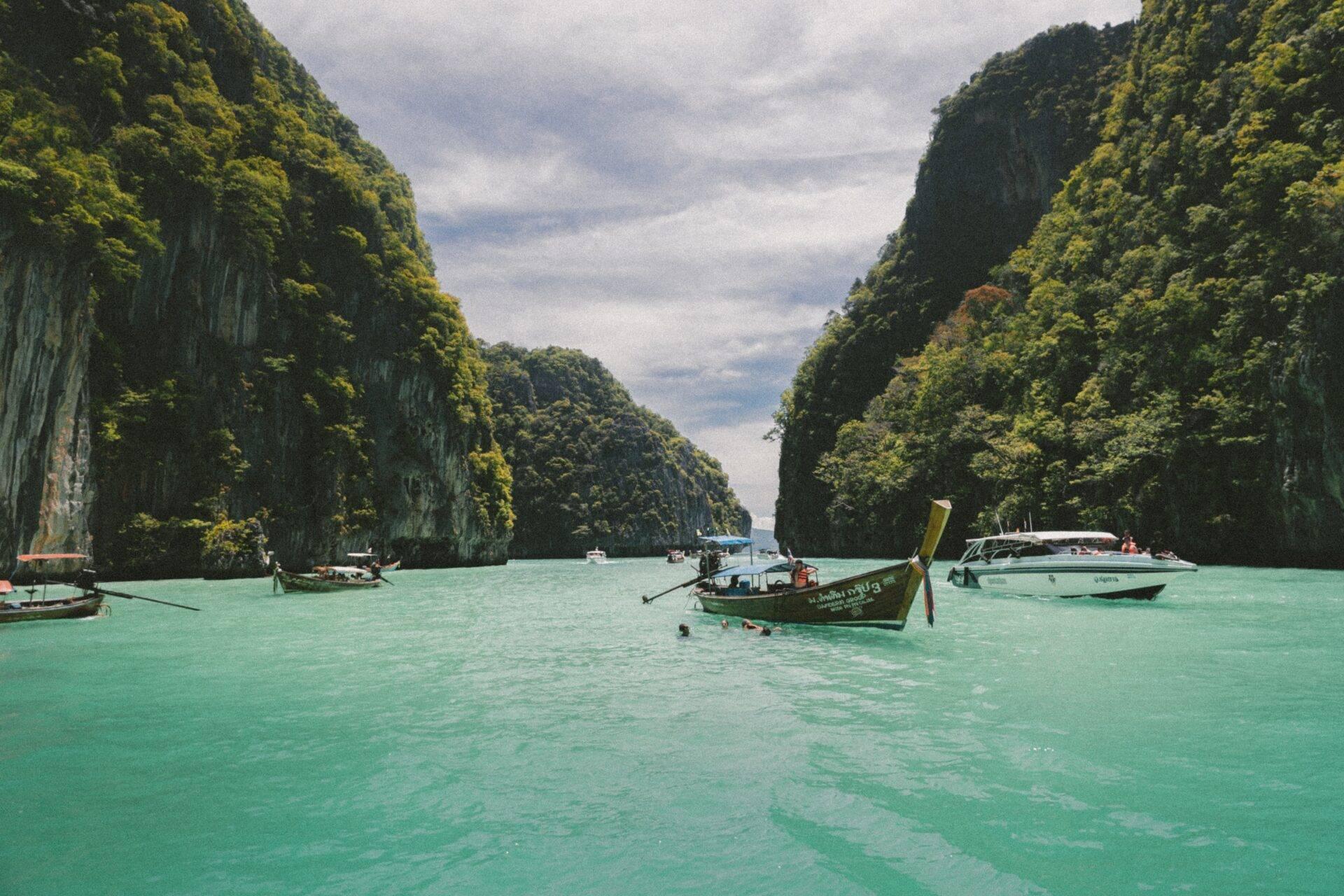 Des bateaux traditionnels ancrés dans une eau turquoise entre deux falaises calcaires densément boisées