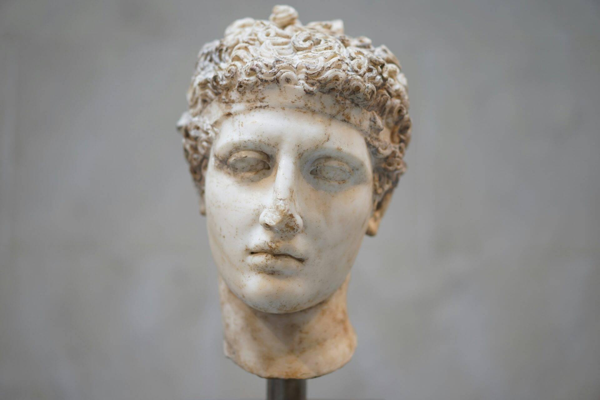 Buste en marbre blanc d’une figure antique aux cheveux bouclés, exposé sur fond gris neutre