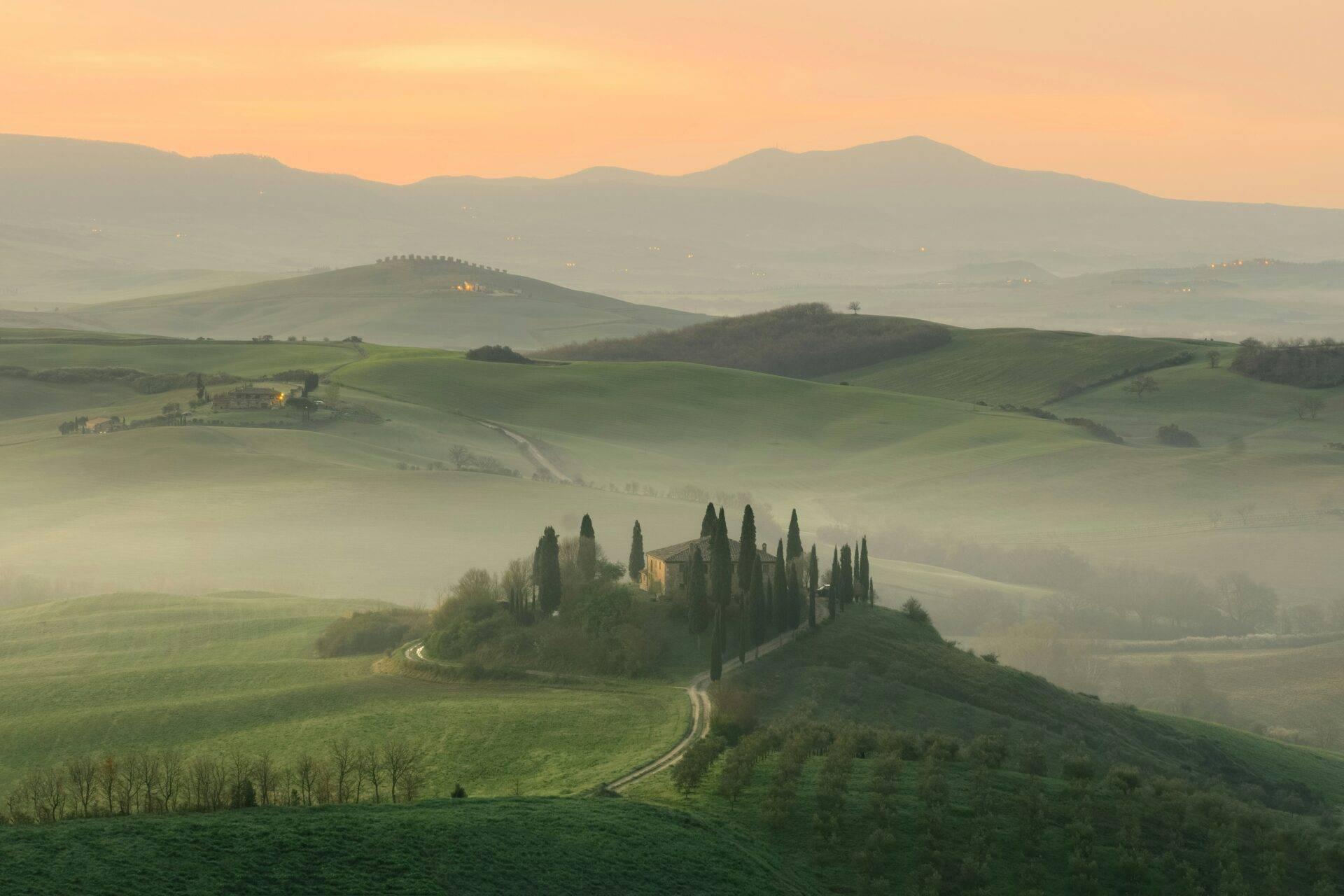 Villa toscana circondata da cipressi all’alba in un paesaggio collinare brumoso