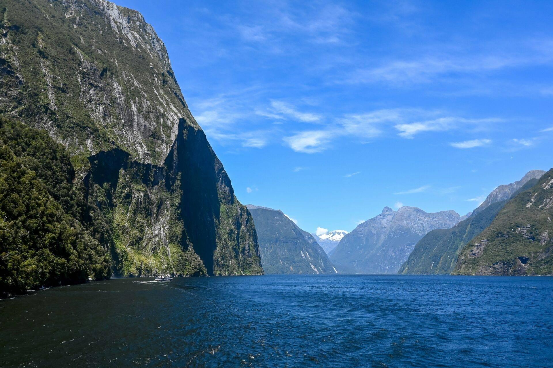Un fjord majestueux encadré de falaises rocheuses vertigineuses et de forêts denses, avec un bateau naviguant sur les eaux bleues