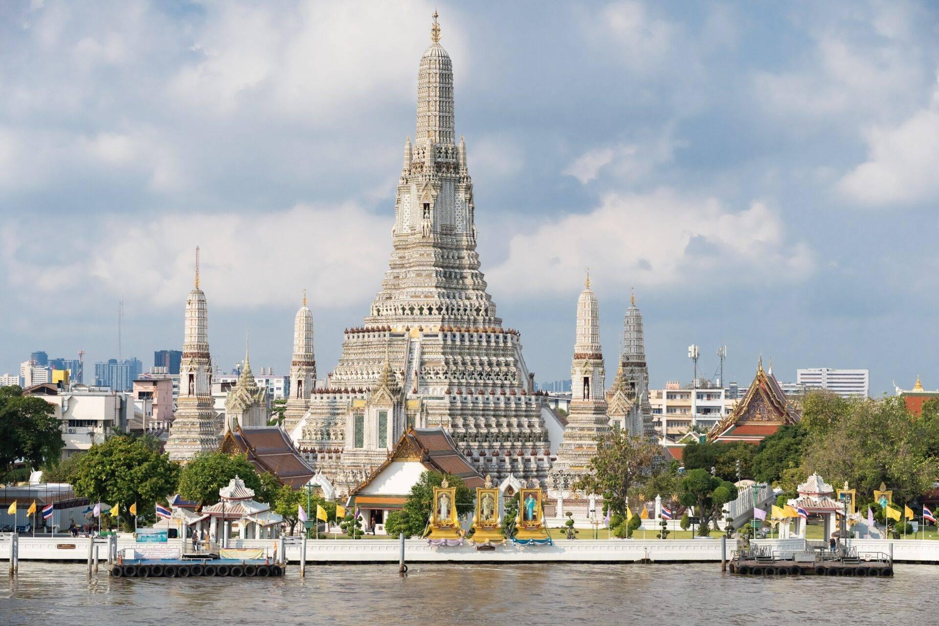 Un majestueux temple bouddhiste blanc et or avec plusieurs stupas pointus se dresse au bord d’une rivière en Thaïlande