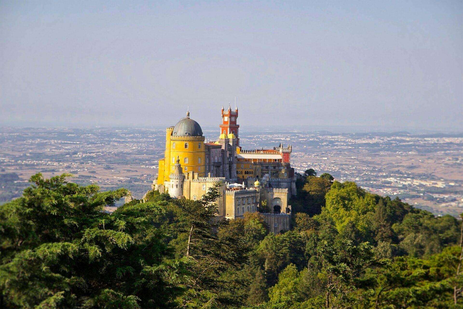 Un maestoso castello colorato arroccato su una collina boscosa che domina una valle verdeggiante