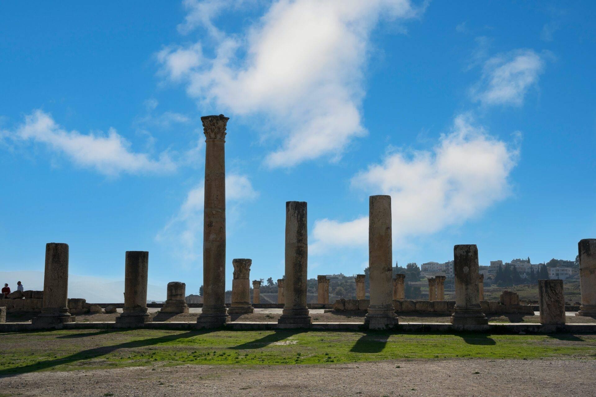 Rovine antiche con colonne di pietra in piedi su un terreno erboso sotto un cielo blu nuvoloso