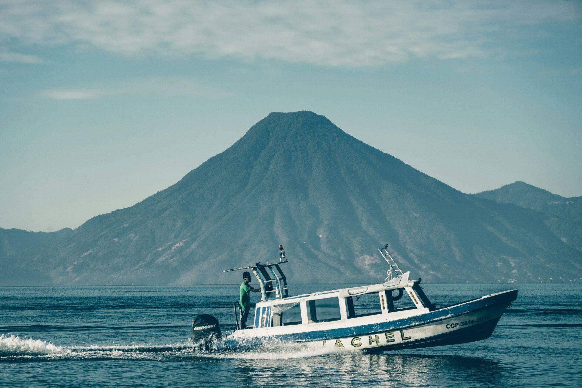 Un bateau de pêche bleu amarré en eaux peu profondes face à un volcan conique majestueux sous ciel dégagé