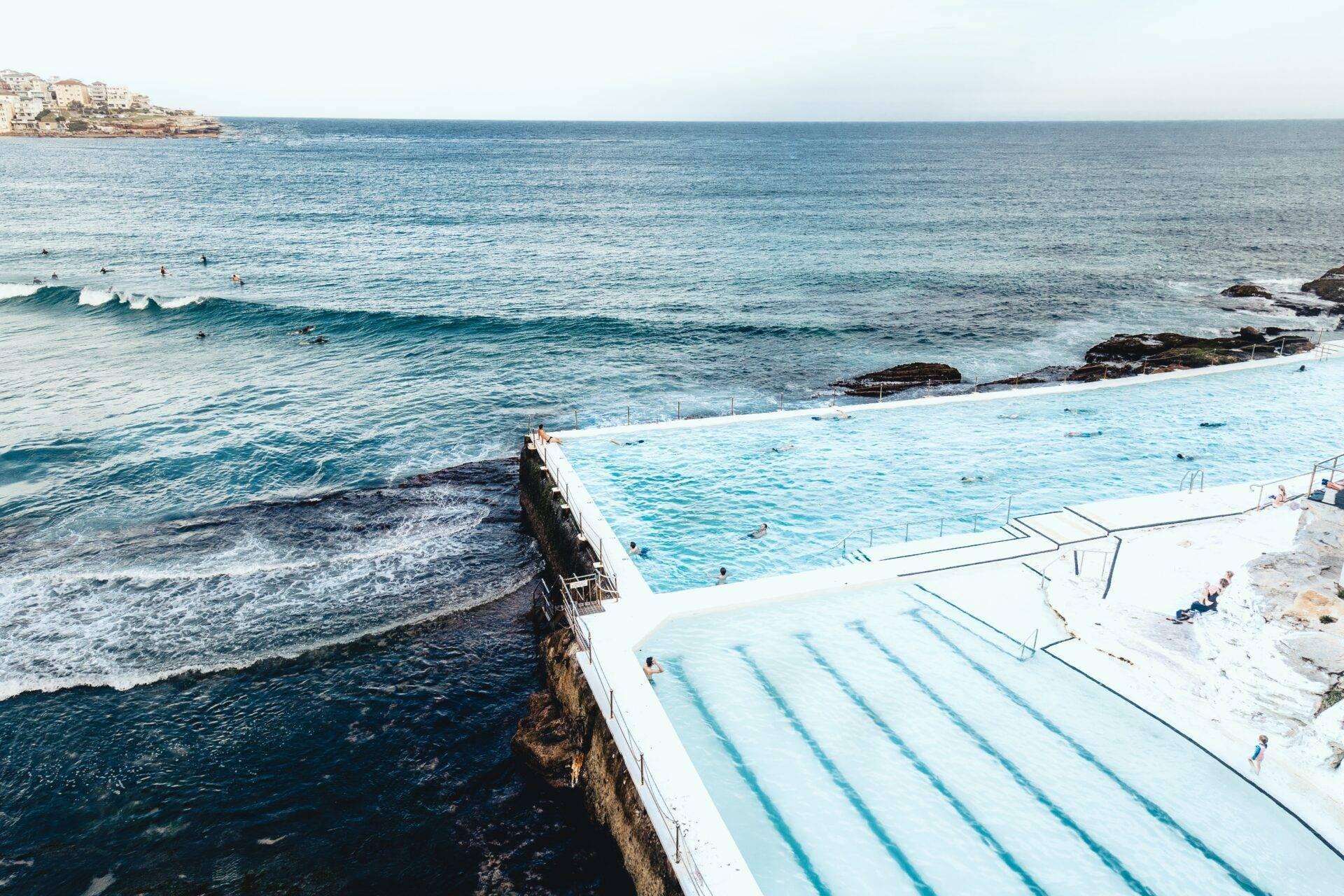 Piscina olímpica al borde del mar con vistas al océano turquesa y una costa rocosa bajo un cielo despejado