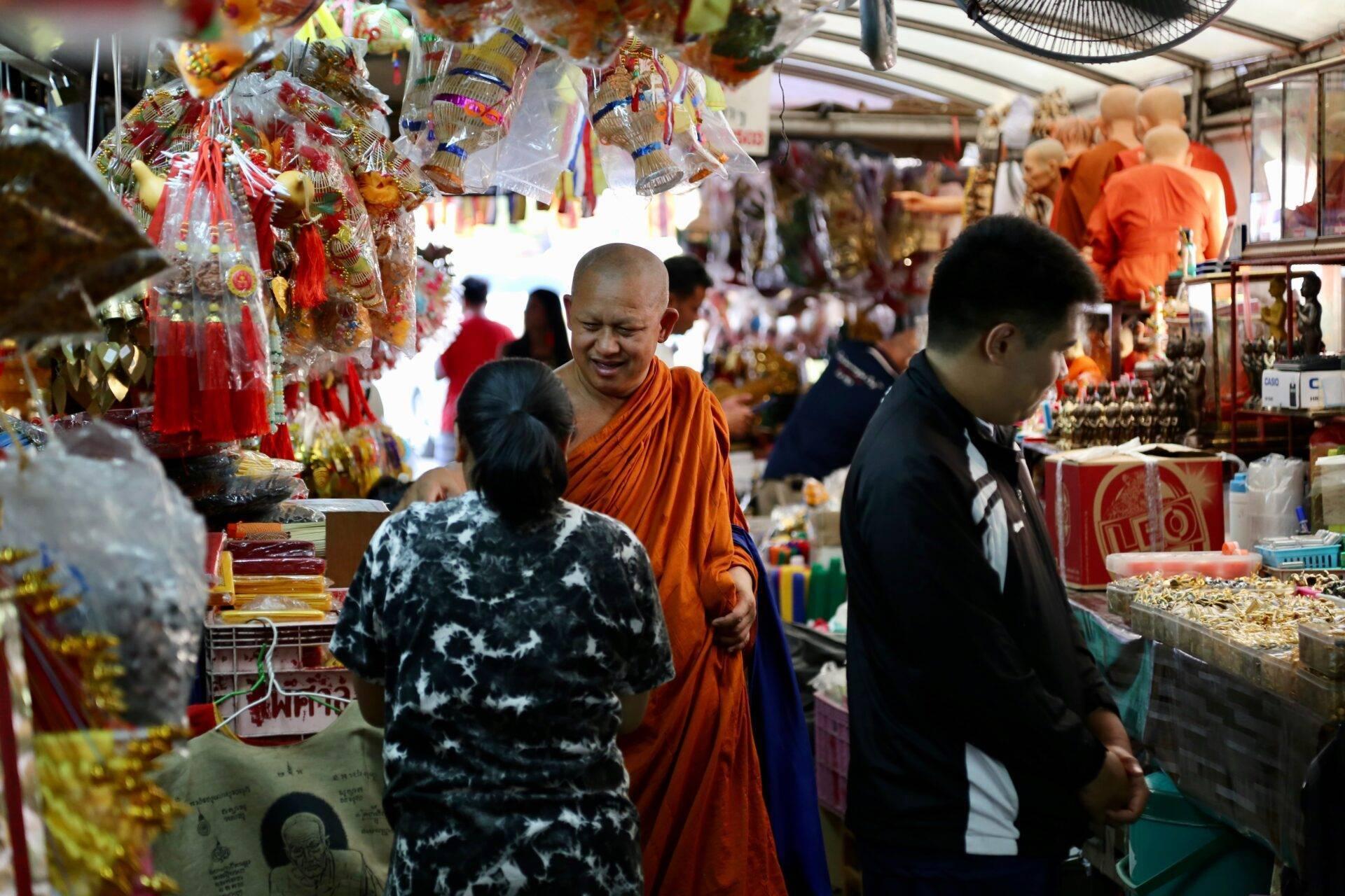 Un moine bouddhiste en robe orange dans un marché couvert rempli de décorations religieuses colorées et de statuettes