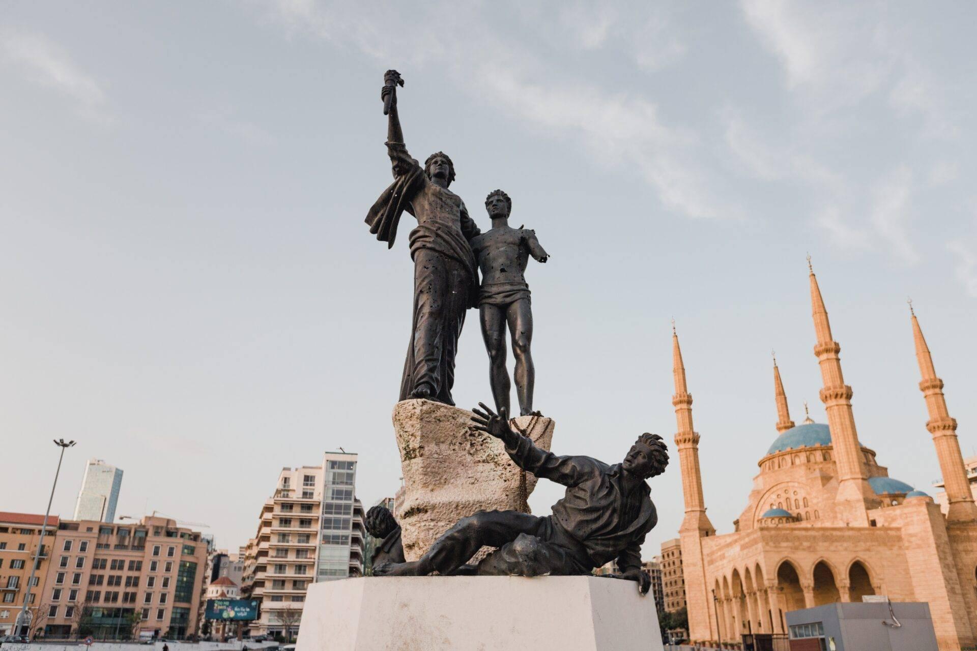 Monument de bronze représentant des figures en lutte avec une mosquée dorée en arrière-plan dans une place urbaine