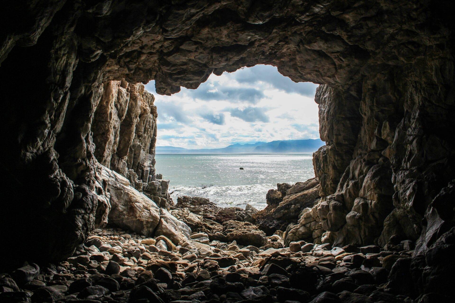 Vista dall’interno di una grotta costiera sul mare, le montagne e un cielo nuvoloso