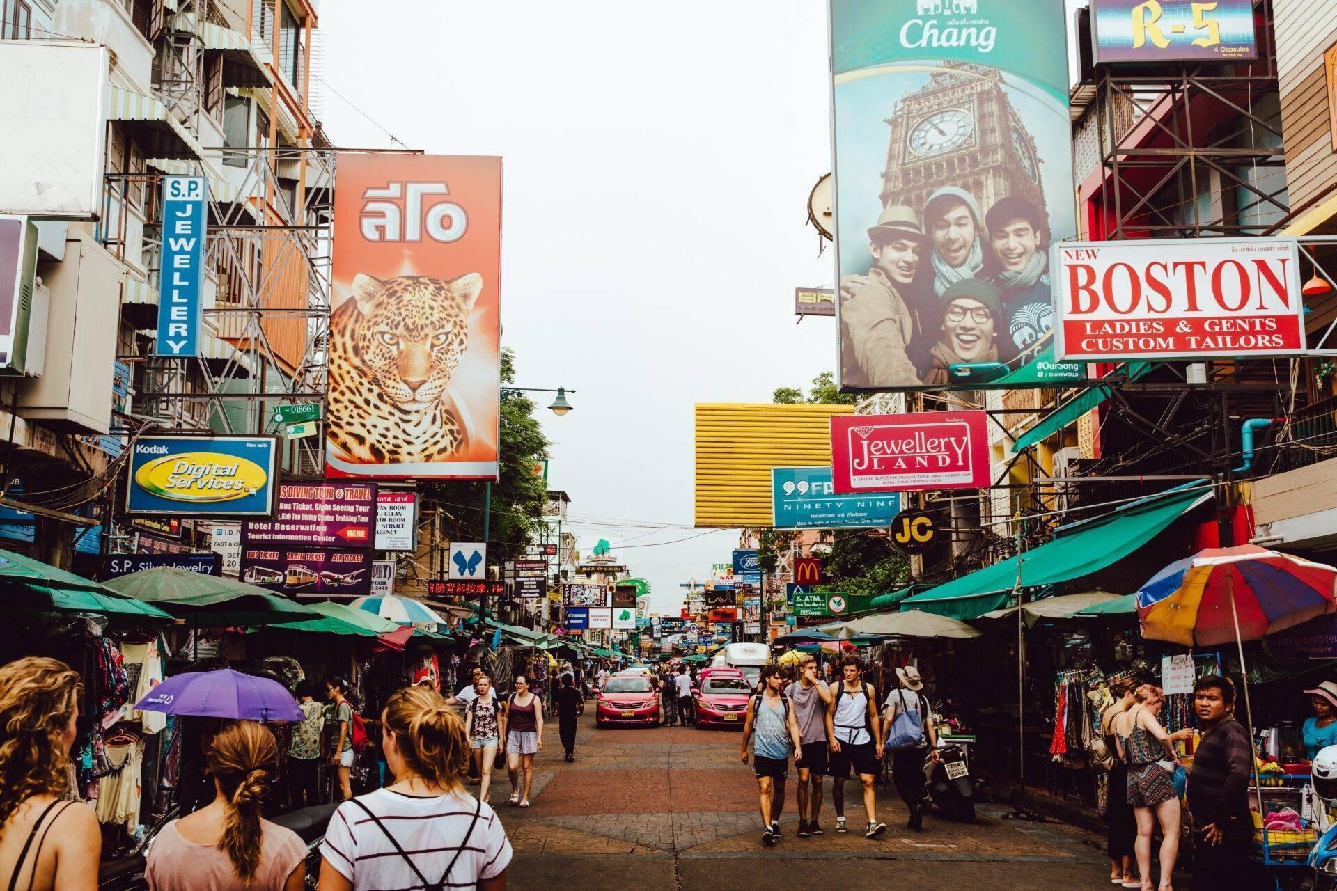 Une rue commerçante animée de Bangkok avec des étals, des enseignes colorées et une foule de touristes et de résidents