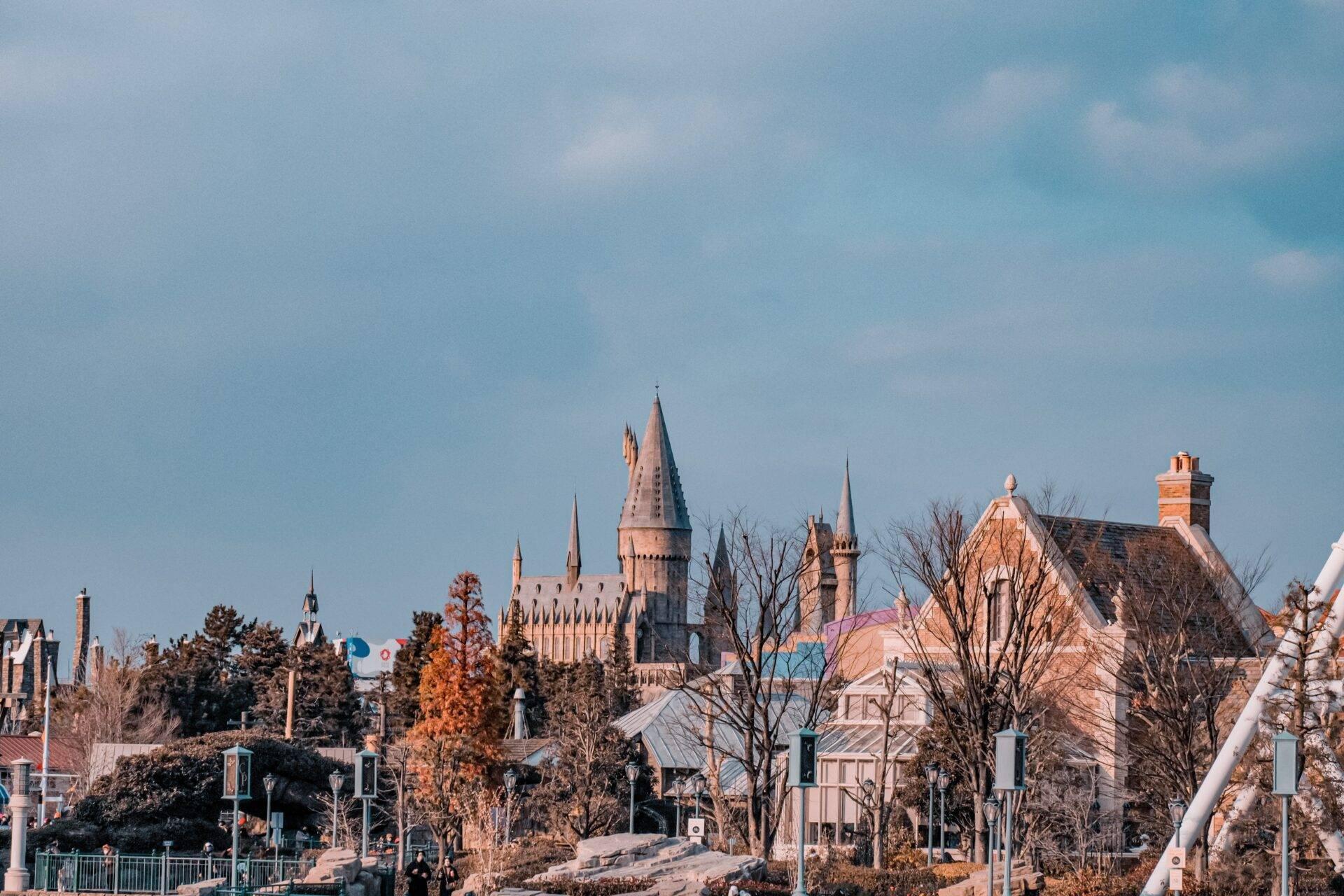Un château de style gothique avec tours pointues entouré de bâtiments colorés et d’arbres en automne sous ciel dégagé