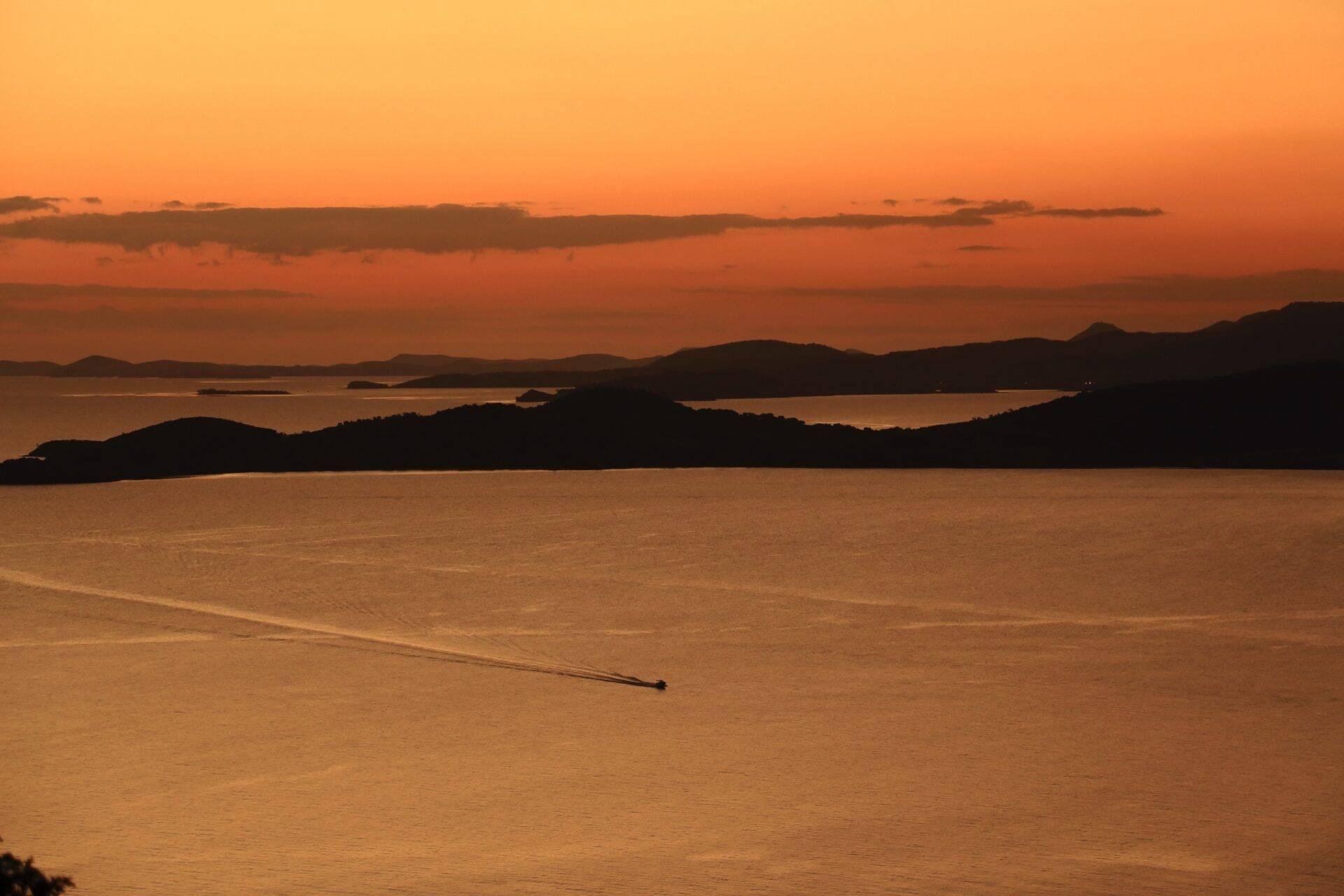 Coucher de soleil doré sur une baie tropicale avec îles boisées et petit bateau naviguant au large