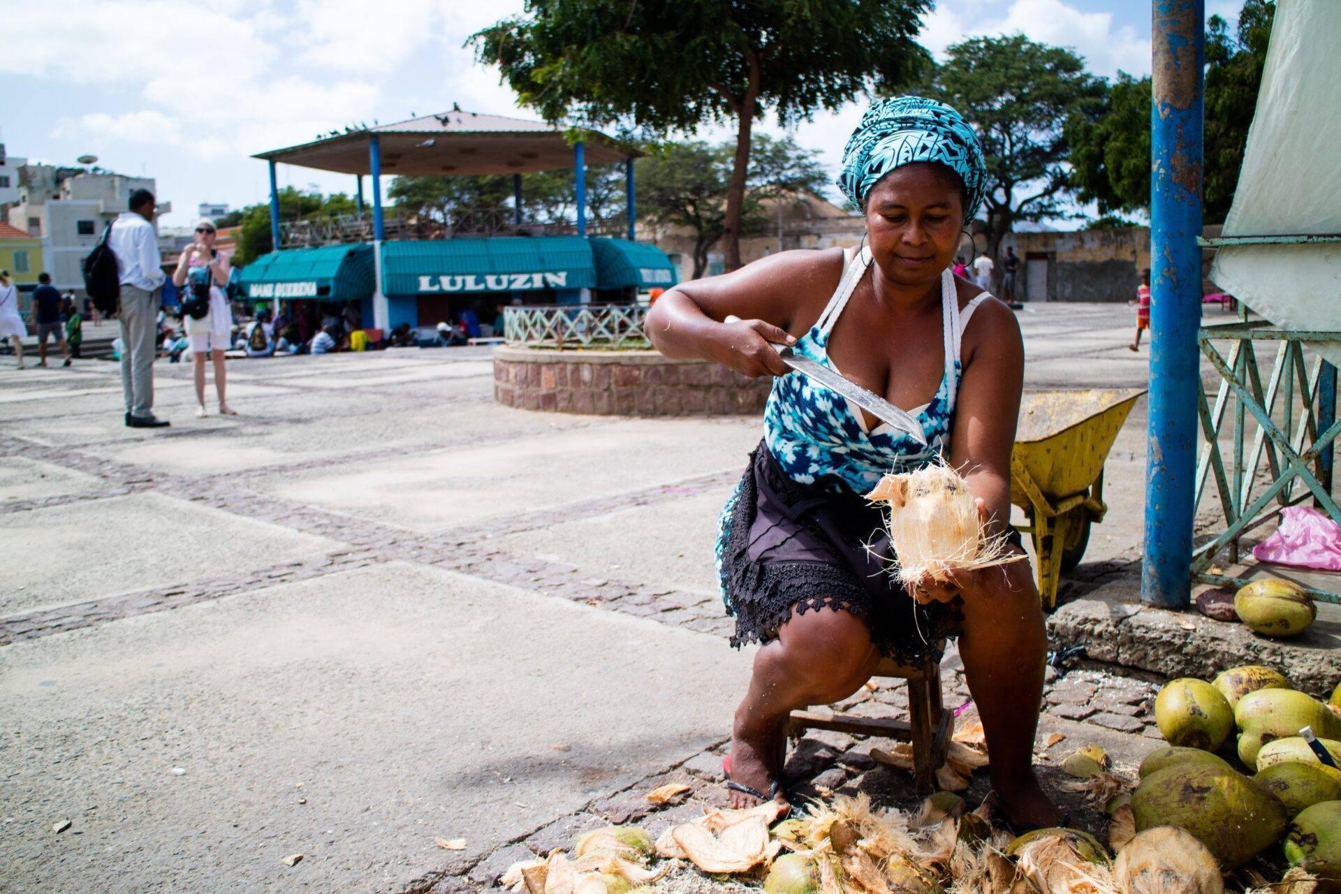 A woman preparing coconuts at an open-air market in a small coastal town