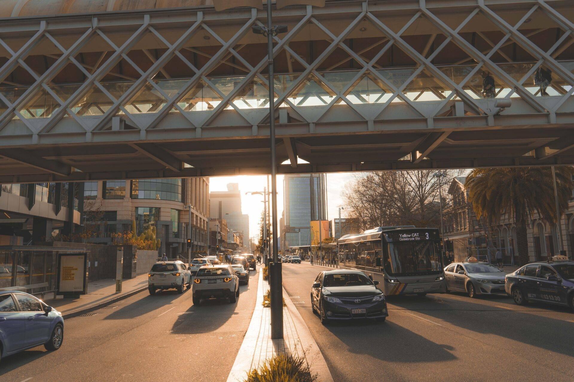 Una calle urbana australiana bajo una estructura de cristal con coches, autobuses y edificios modernos al atardecer