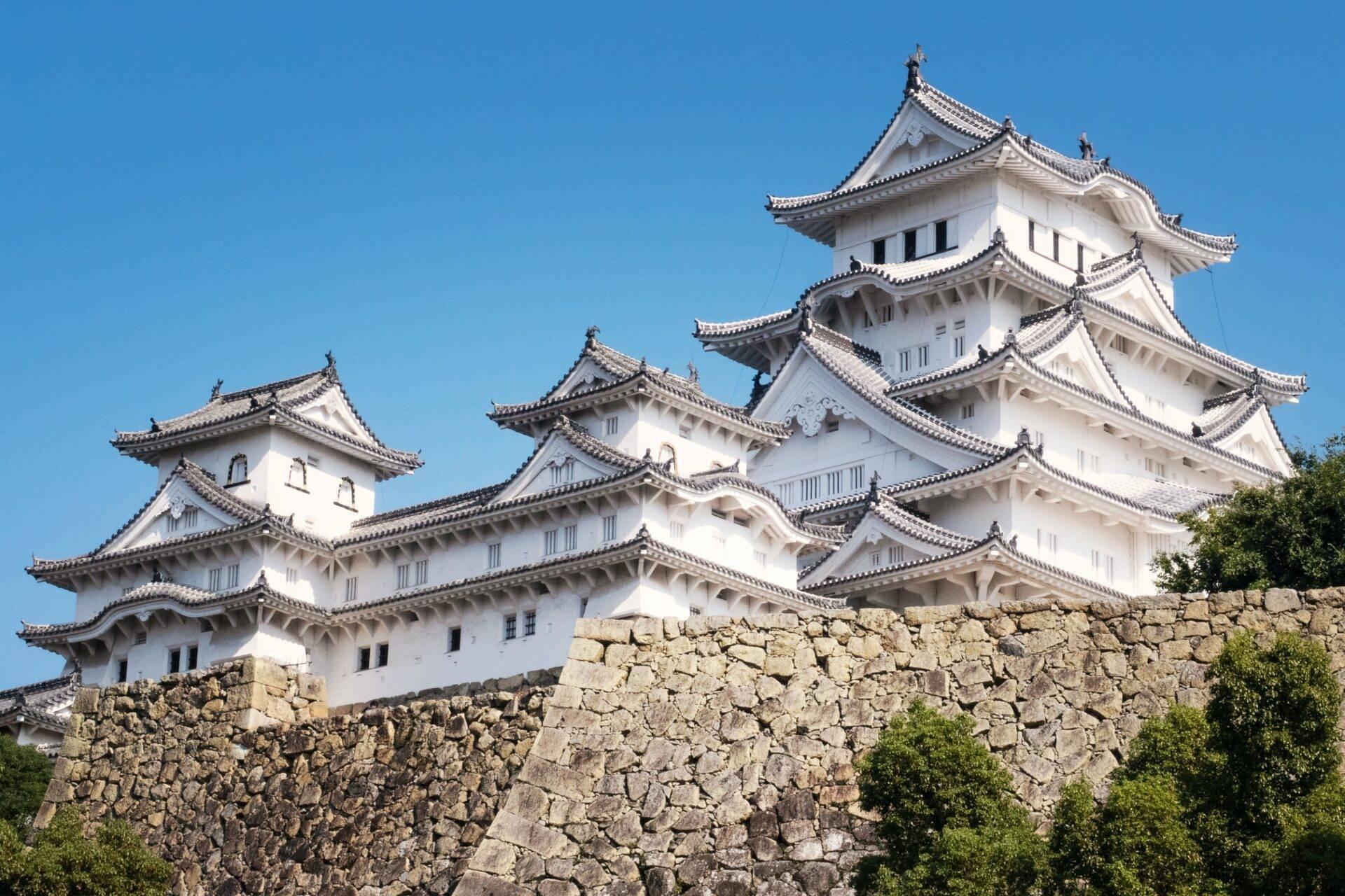Un château japonais blanc aux toits courbes avec des tuiles noires sur une muraille en pierre sous ciel bleu