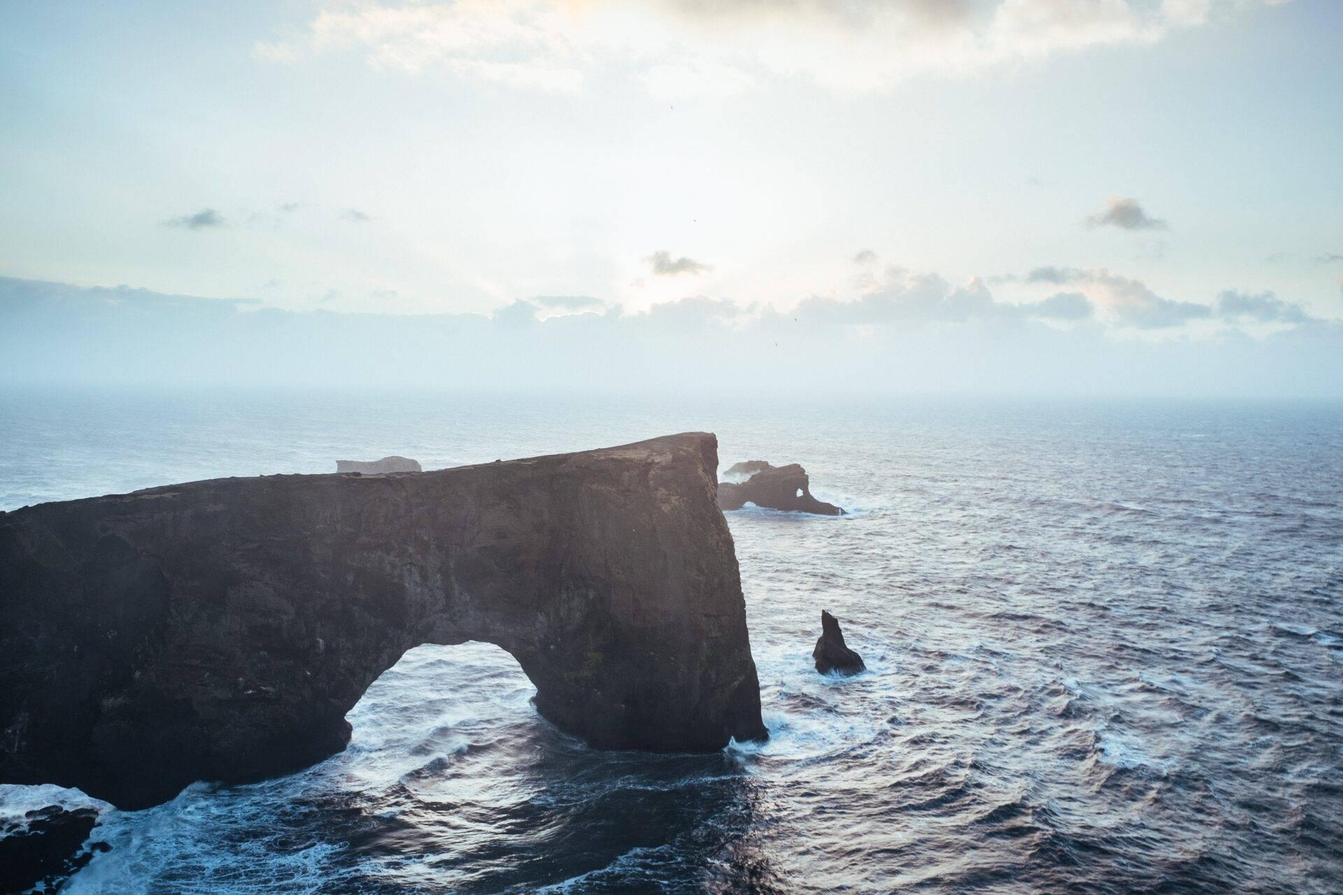 Scogliera rocciosa nera con arco naturale che domina l’oceano in tempesta sotto un cielo nuvoloso