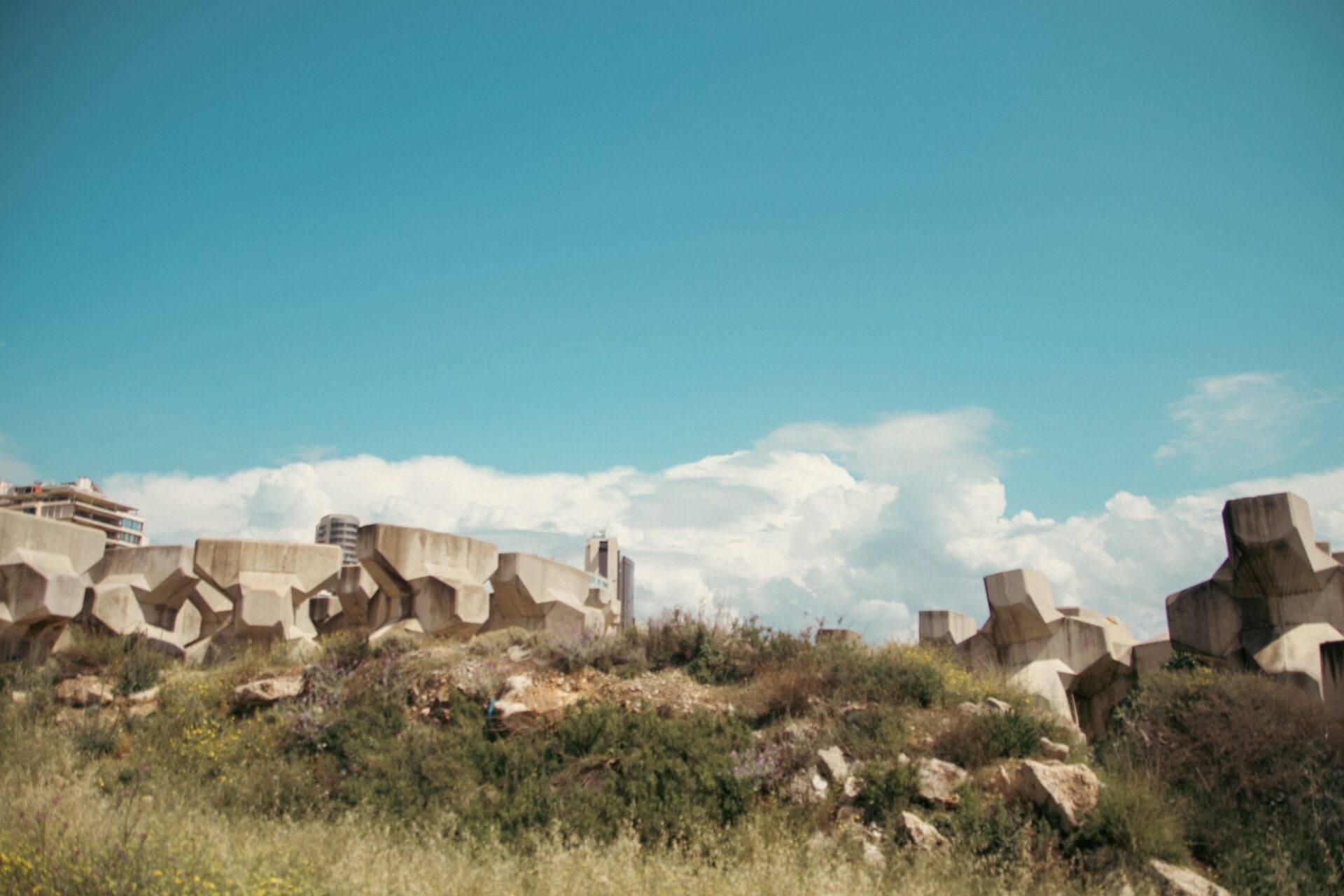 Des ruines de béton monumental avec blocs géométriques sur une colline rocheuse sous ciel bleu