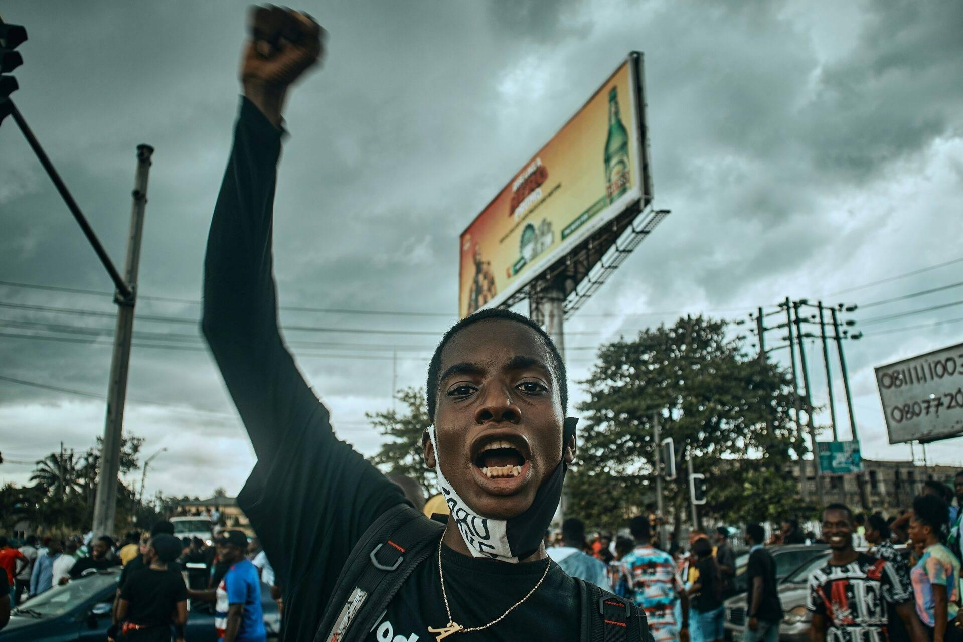 Un uomo alza il pugno durante una manifestazione animata in una via cittadina sotto un cielo nuvoloso