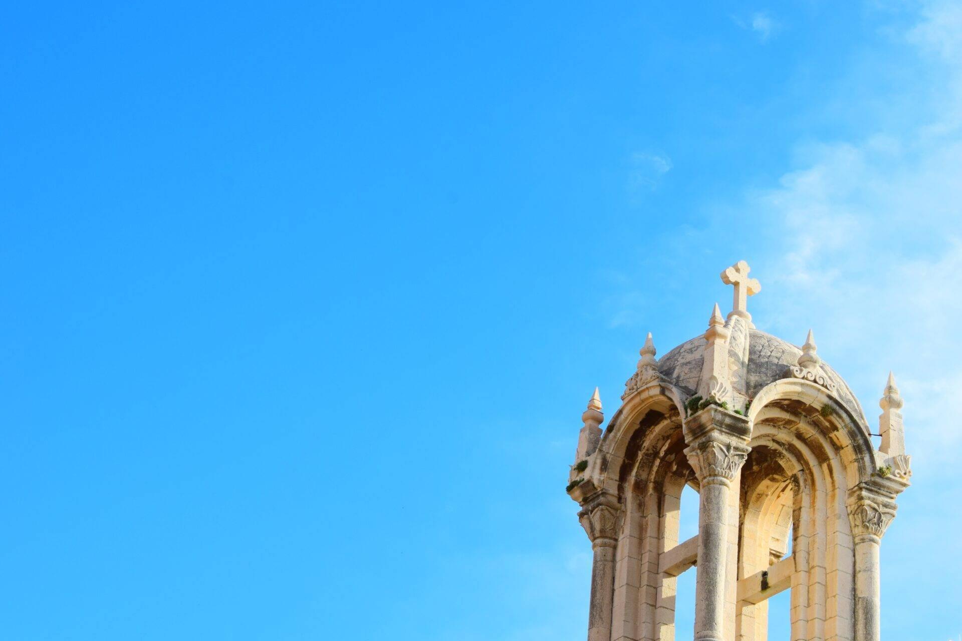 Chapelle chrétienne en ruines avec colonnes ornées et croix dorée au sommet, ciel bleu dégagé