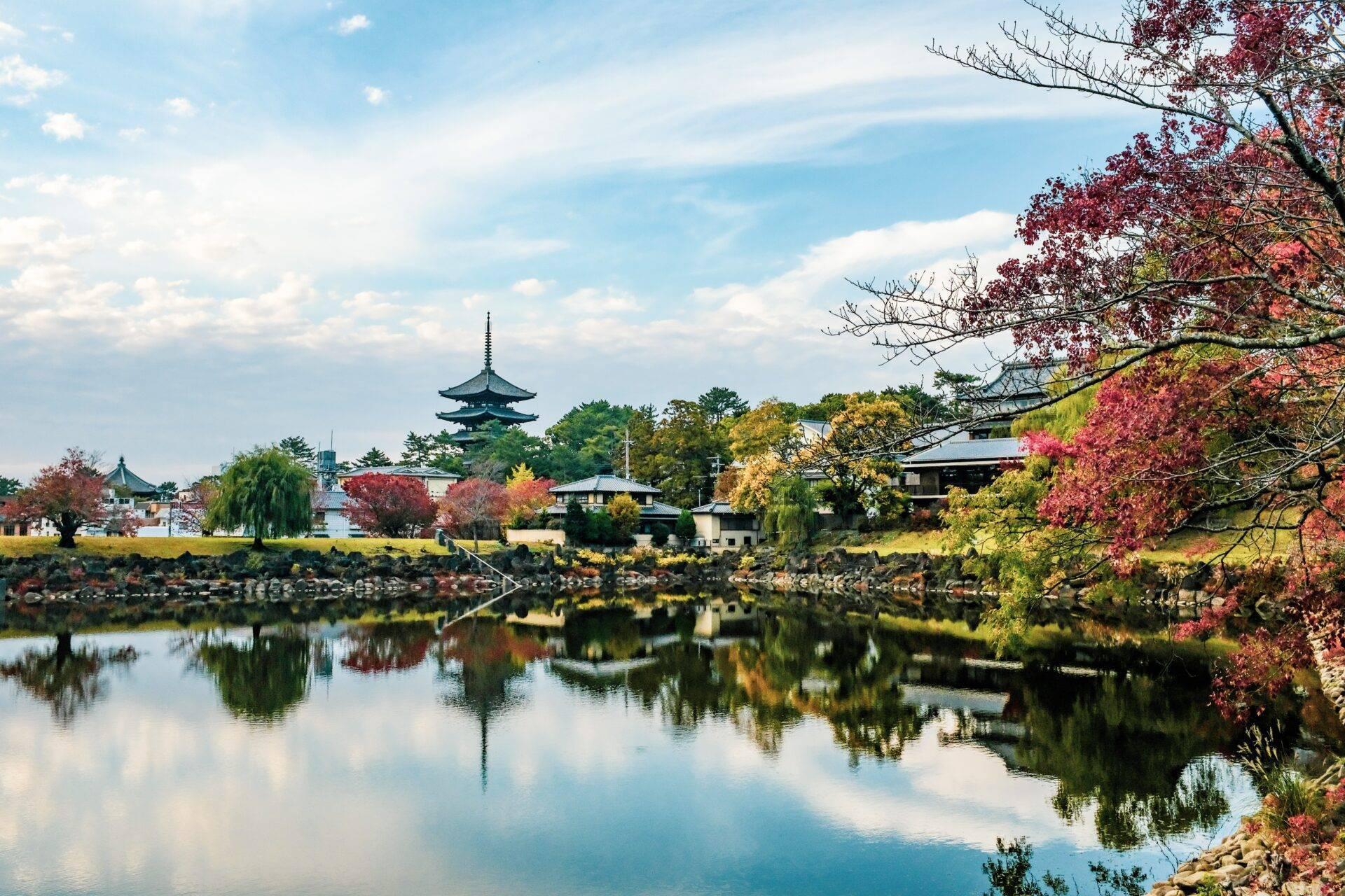 Paysage automnal japonais avec un temple traditionnel se reflétant dans une rivière calme entourée d’arbres aux feuillages rouges et dorés
