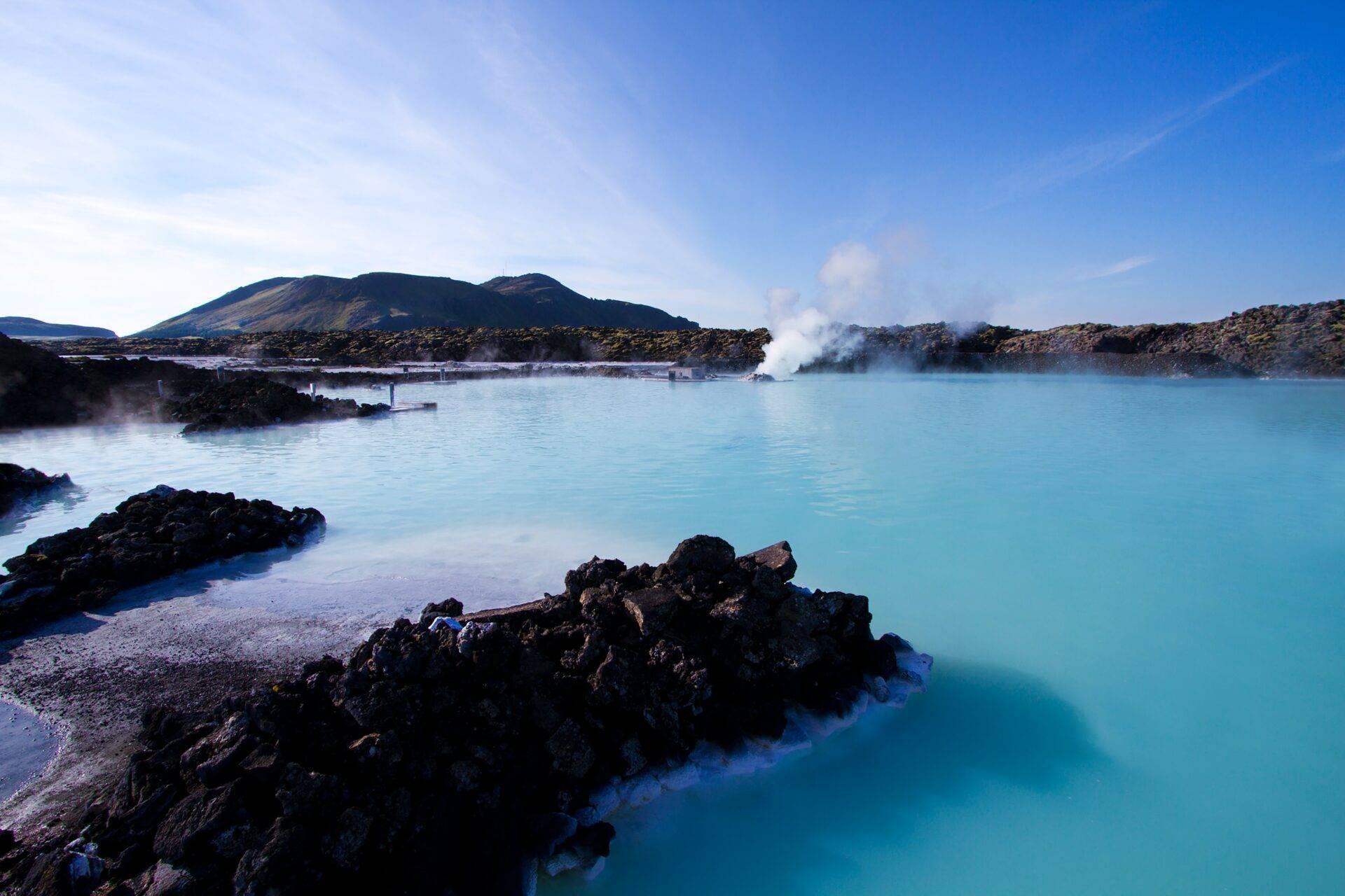 Laguna geotermica dalle acque turchesi circondata da rocce vulcaniche nere e vapori caldi