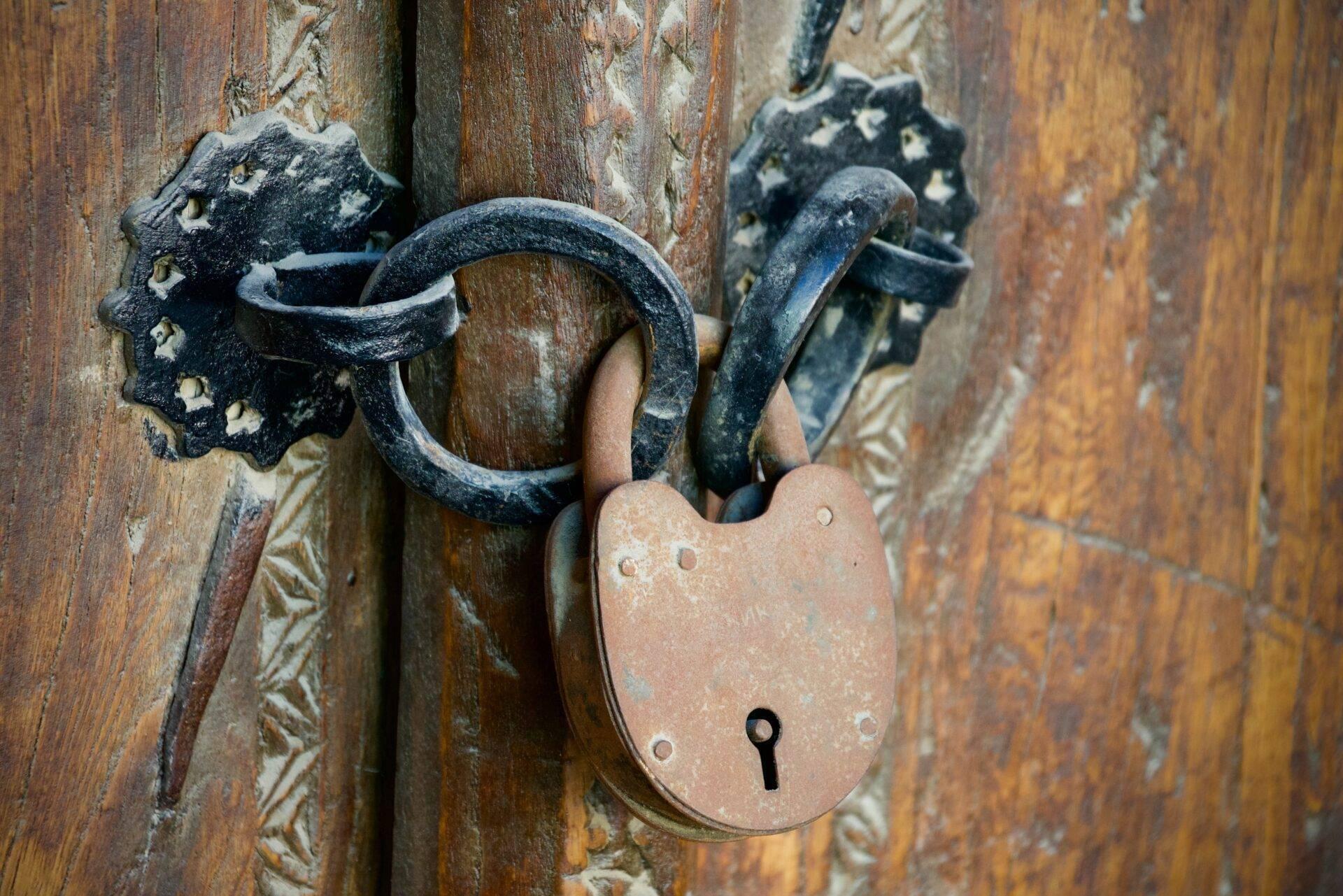 Un vieux cadenas en cuivre et une serrure forgée noire ornementale sur une porte en bois patinée