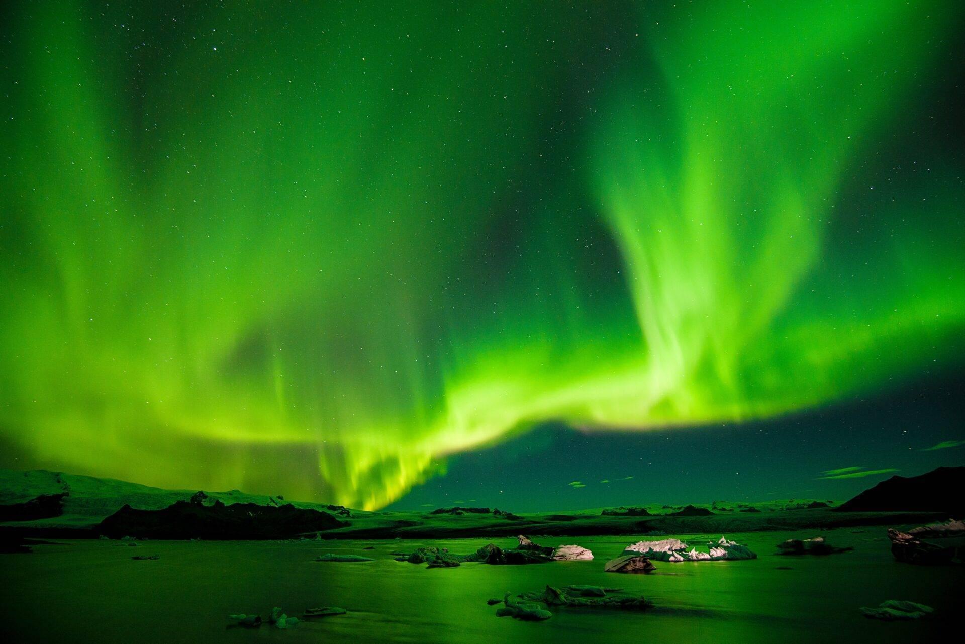 Aurore boréale verte spectaculaire dansant au-dessus d’un paysage glacé avec rochers et montagnes en arrière-plan