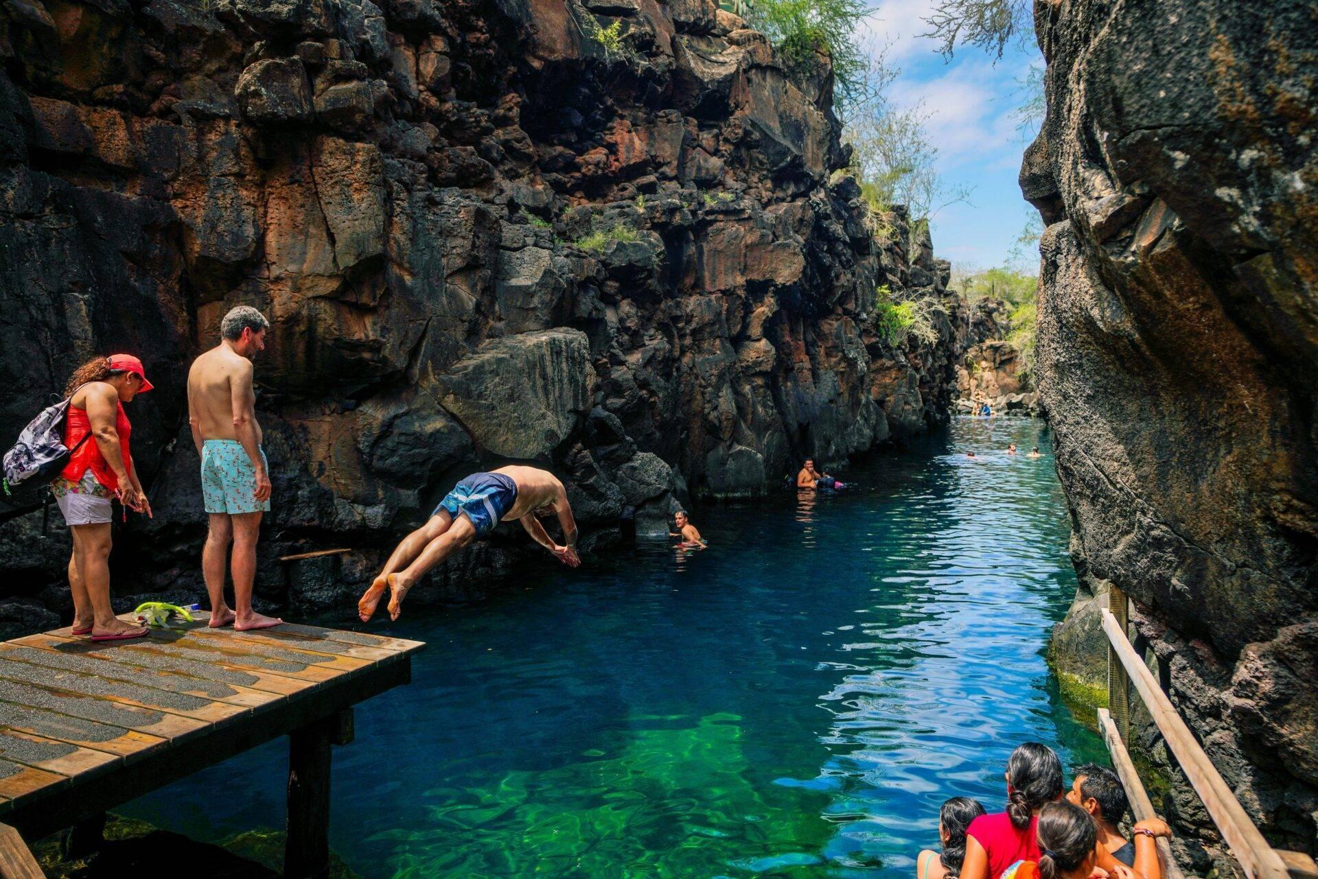 Des touristes plongent dans une piscine naturelle cristalline encadrée par des falaises rocheuses escarpées