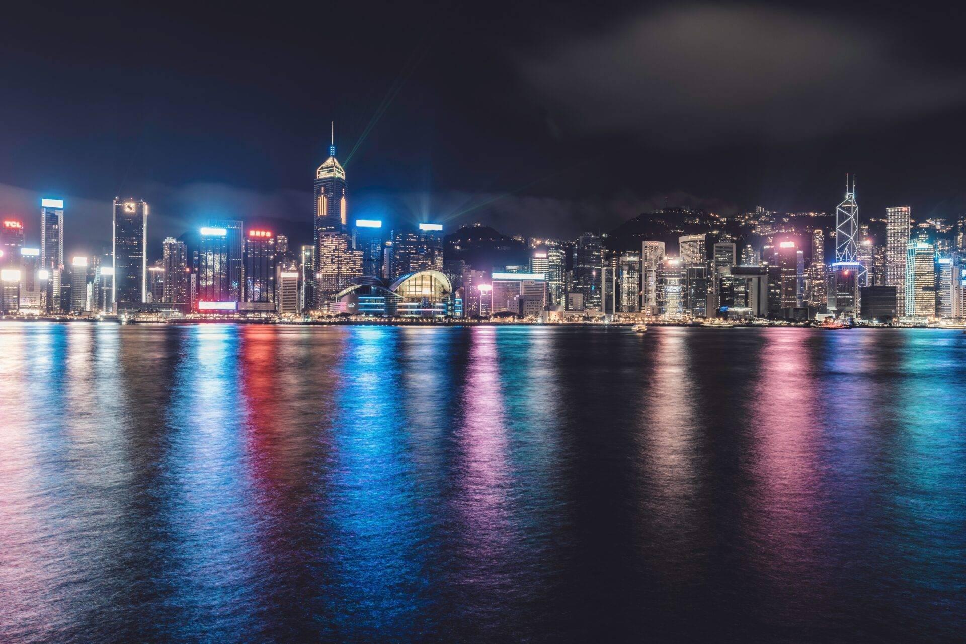 Skyline illuminé d’une métropole côtière la nuit, avec gratte-ciel reflétés dans une baie calme