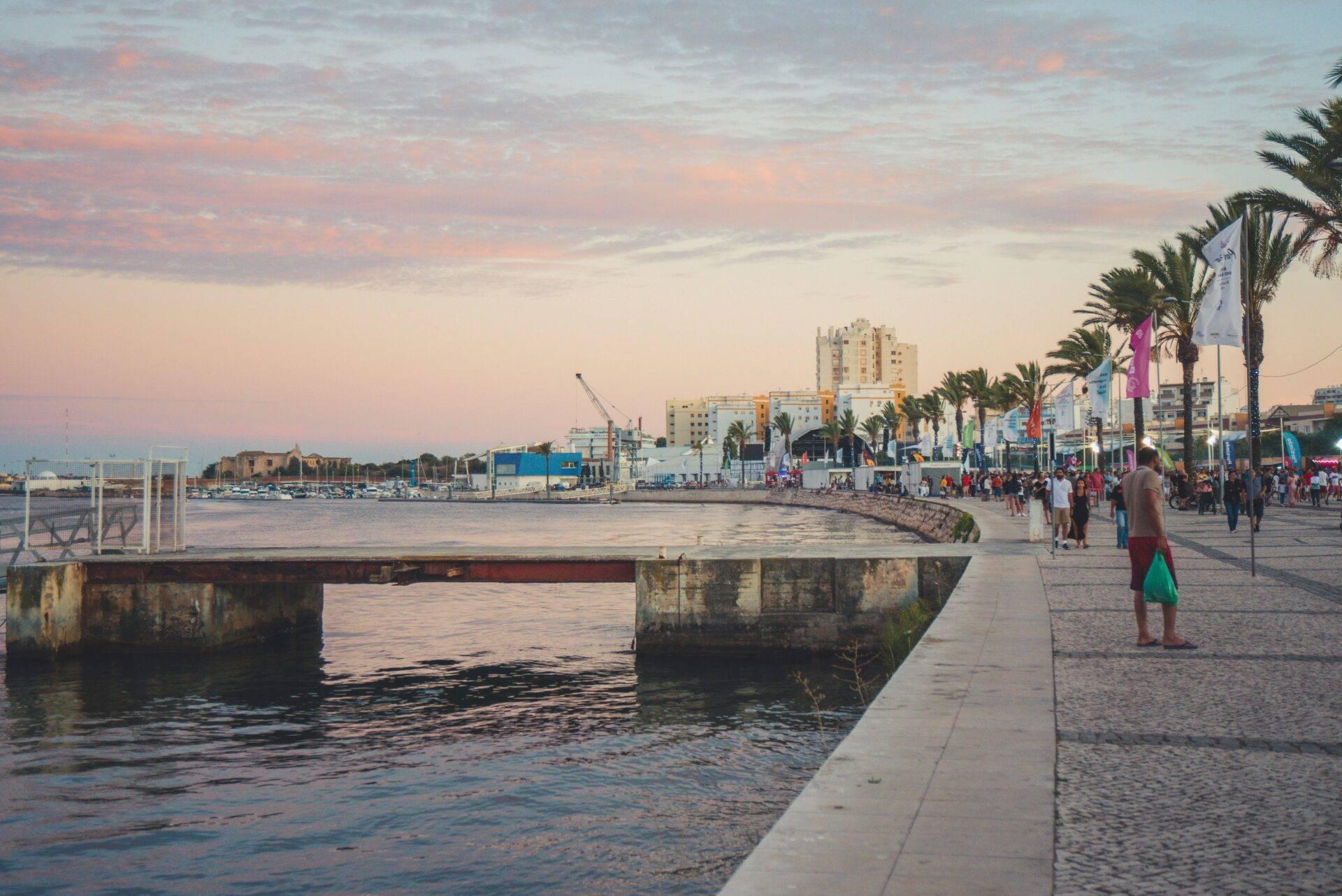 Una vivace passeggiata costiera al tramonto con palme, architettura moderna e porto marittimo sullo sfondo