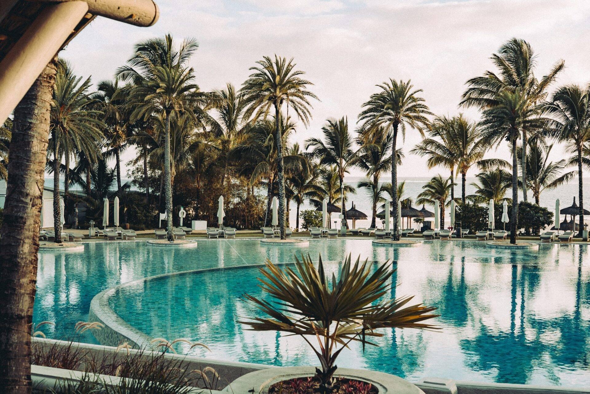 Ein großer türkisfarbener Pool gesäumt von Palmen und weißen Liegestühlen in einem luxuriösen Tropenresort