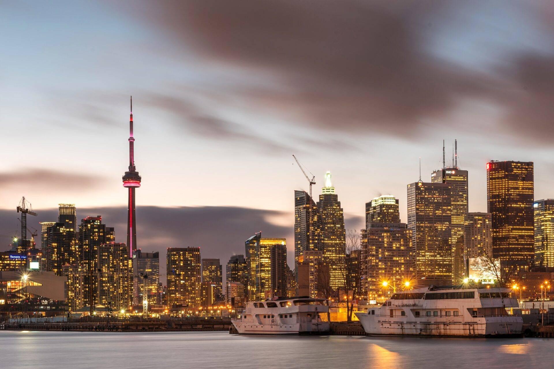 Skyline urbain au crépuscule avec gratte-ciels illuminés, tour de télécommunication distinctive et bateaux amarrés au port