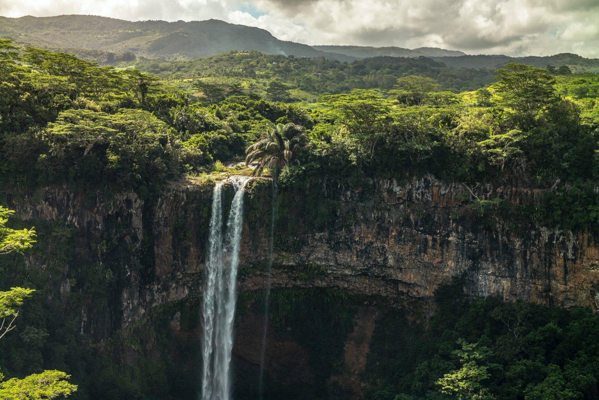 Ein spektakulärer Wasserfall stürzt von einer Basaltklippe in ein üppiges tropisches Tal, umgeben von bewaldeten Bergen