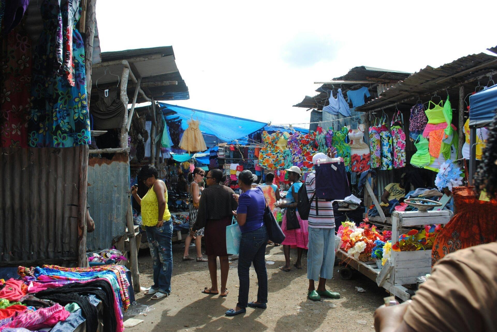 Un mercato all’aperto con abiti e tessuti dai colori vivaci esposti, visitatori che passeggiano tra le bancarelle