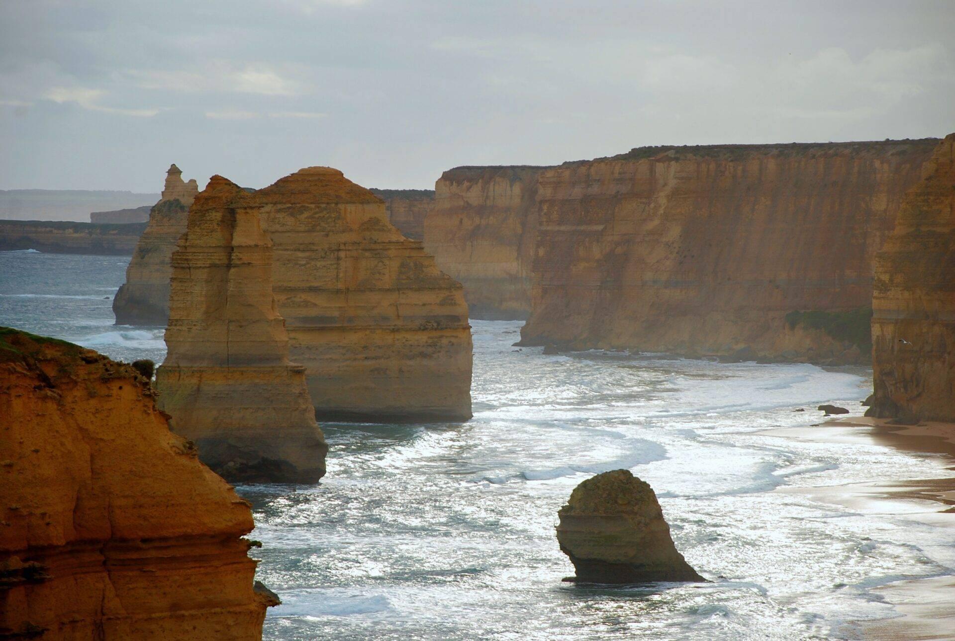 Imponentes formaciones rocosas costeras que emergen del océano bajo un cielo nublado con playa de arena