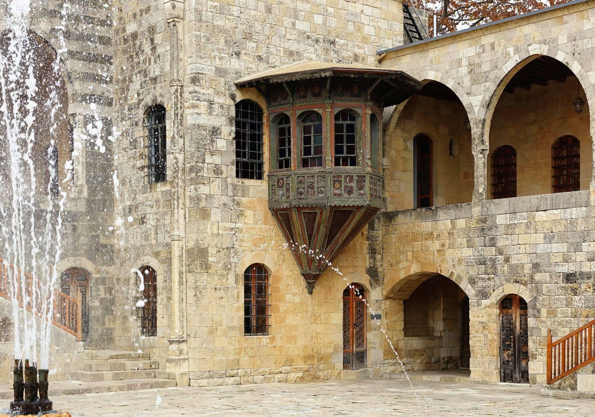 Cour intérieure d’une forteresse médiévale avec arcades en pierre, fenêtres ornementées et balcon suspendu décoré