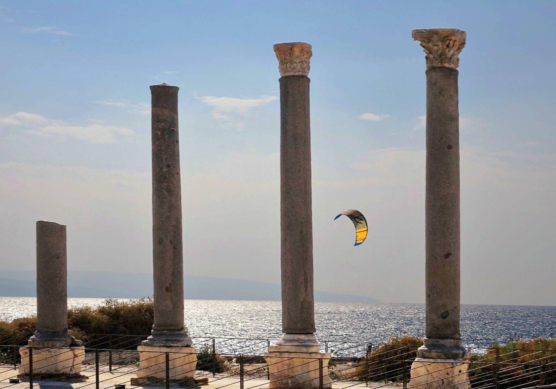 Quatre colonnes romaines antiques face à la mer avec un cerf-volant de kite surf en arrière-plan