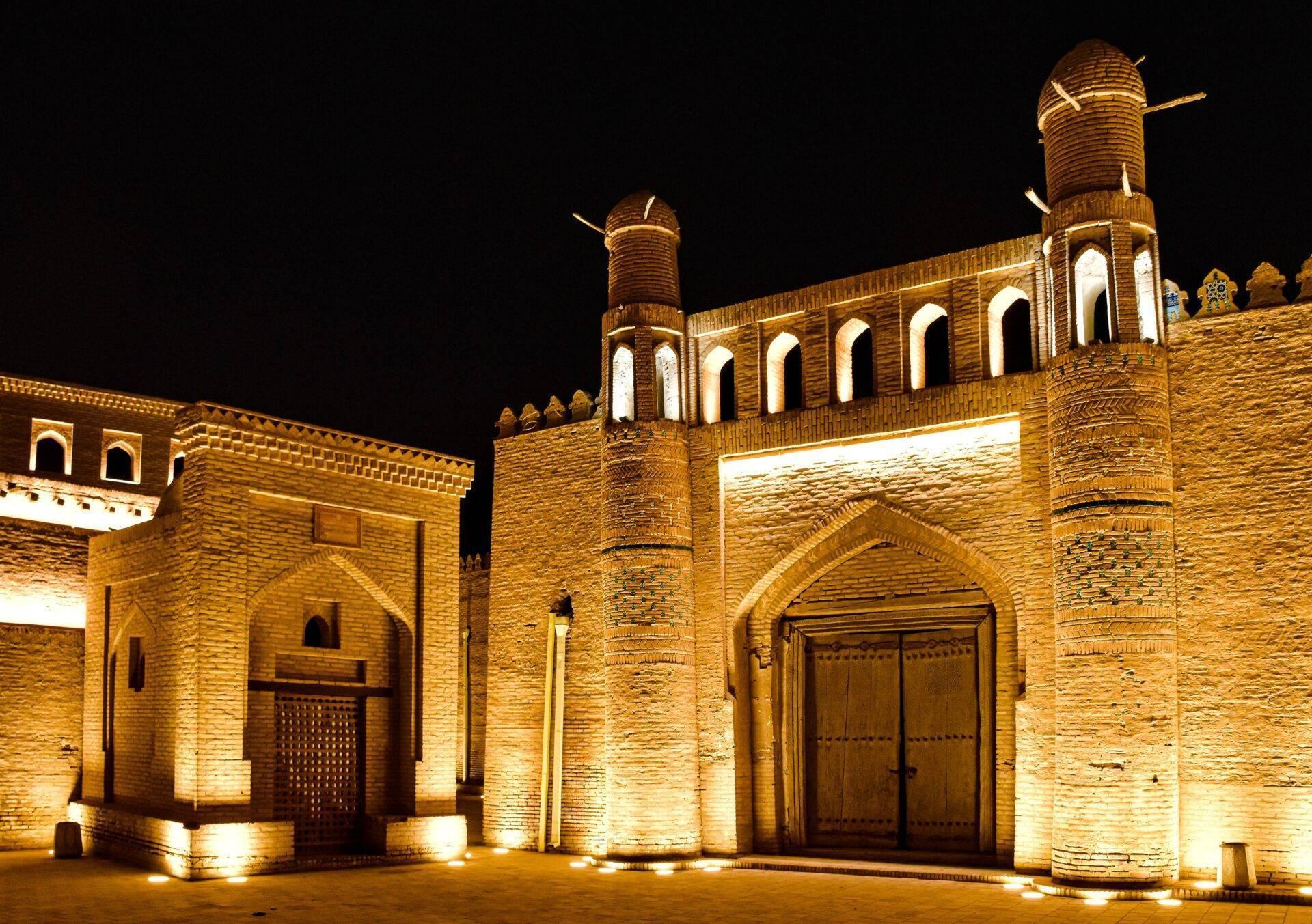 Mosquée historique en briques illuminée la nuit avec minarets et arcade architecturale caractéristique de l’Asie centrale