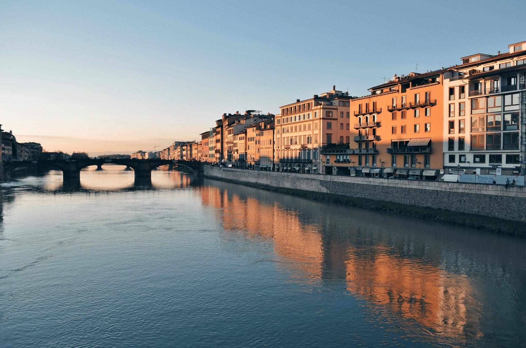 Bâtiments historiques aux façades ocre se reflétant dans un fleuve avec pont voûté au coucher du soleil