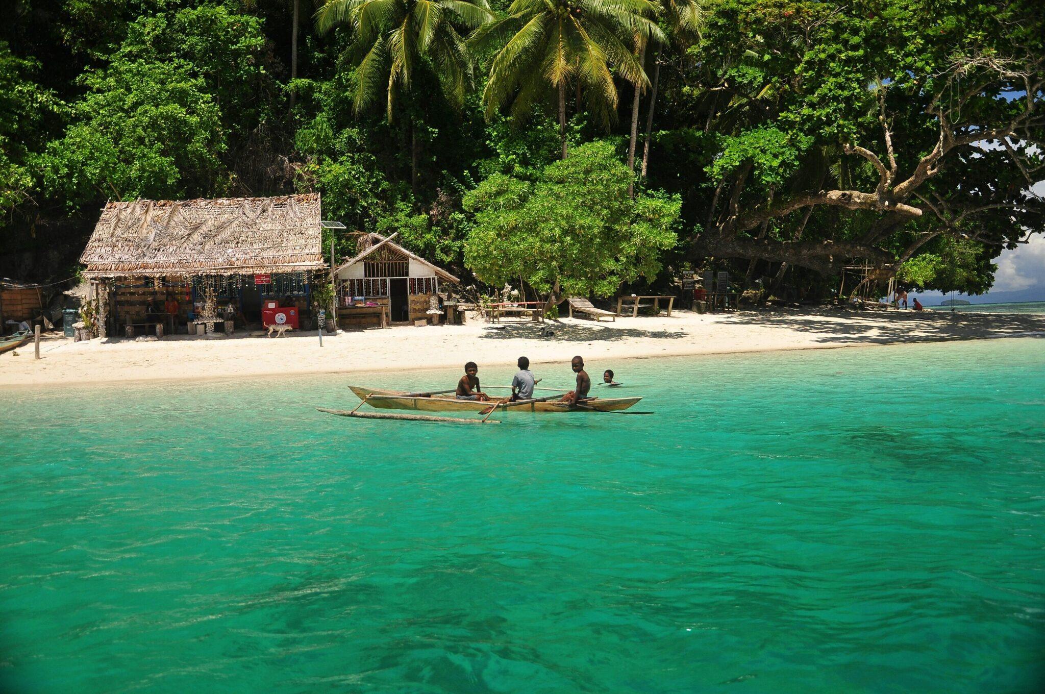 Petite embarcation traditionnelle avec passagers en eaux turquoise devant des bungalows en paille et plage de sable blanc