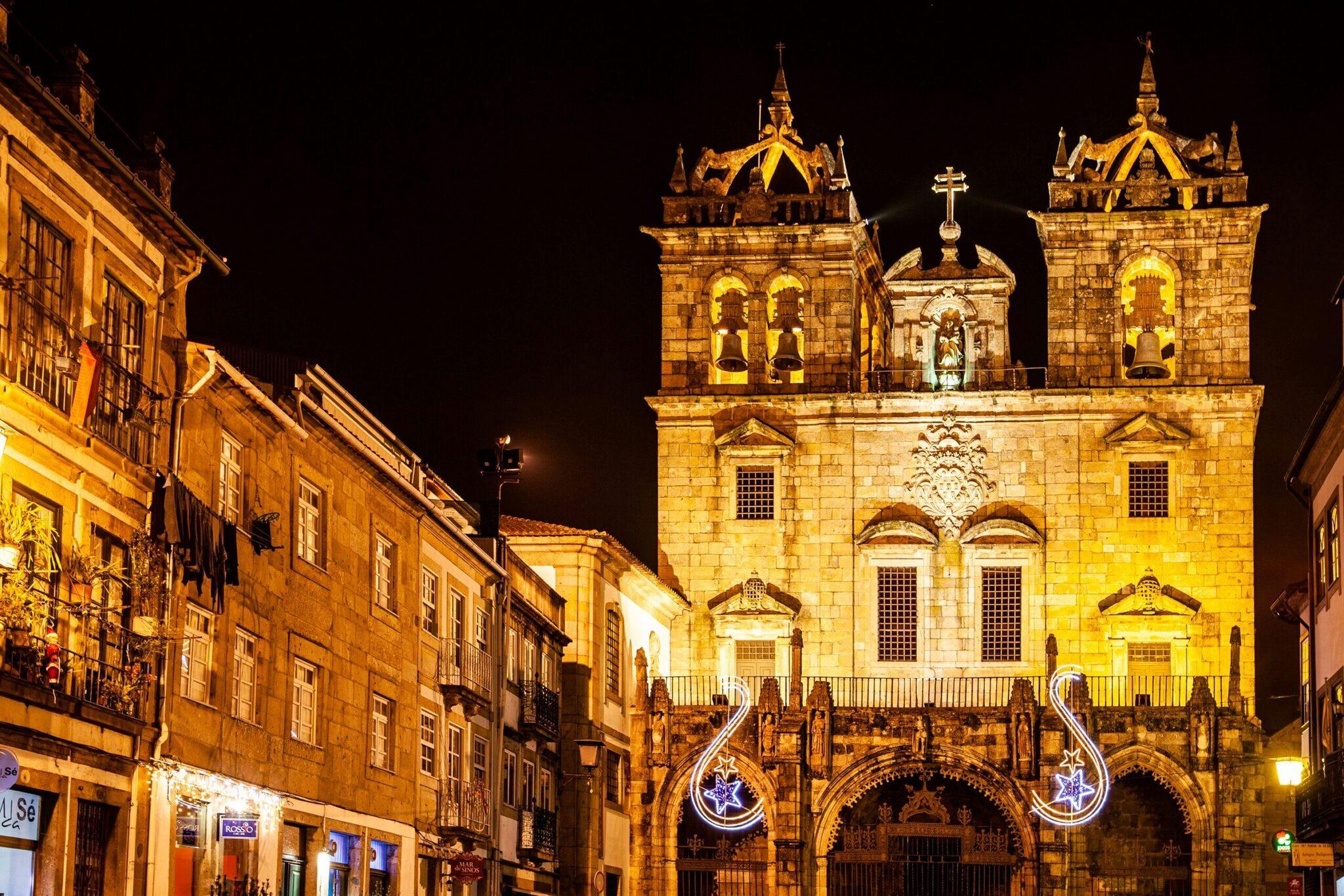 Illuminated facade of a baroque church with two towers, decorated with festive light motifs, flanked by historic stone buildings