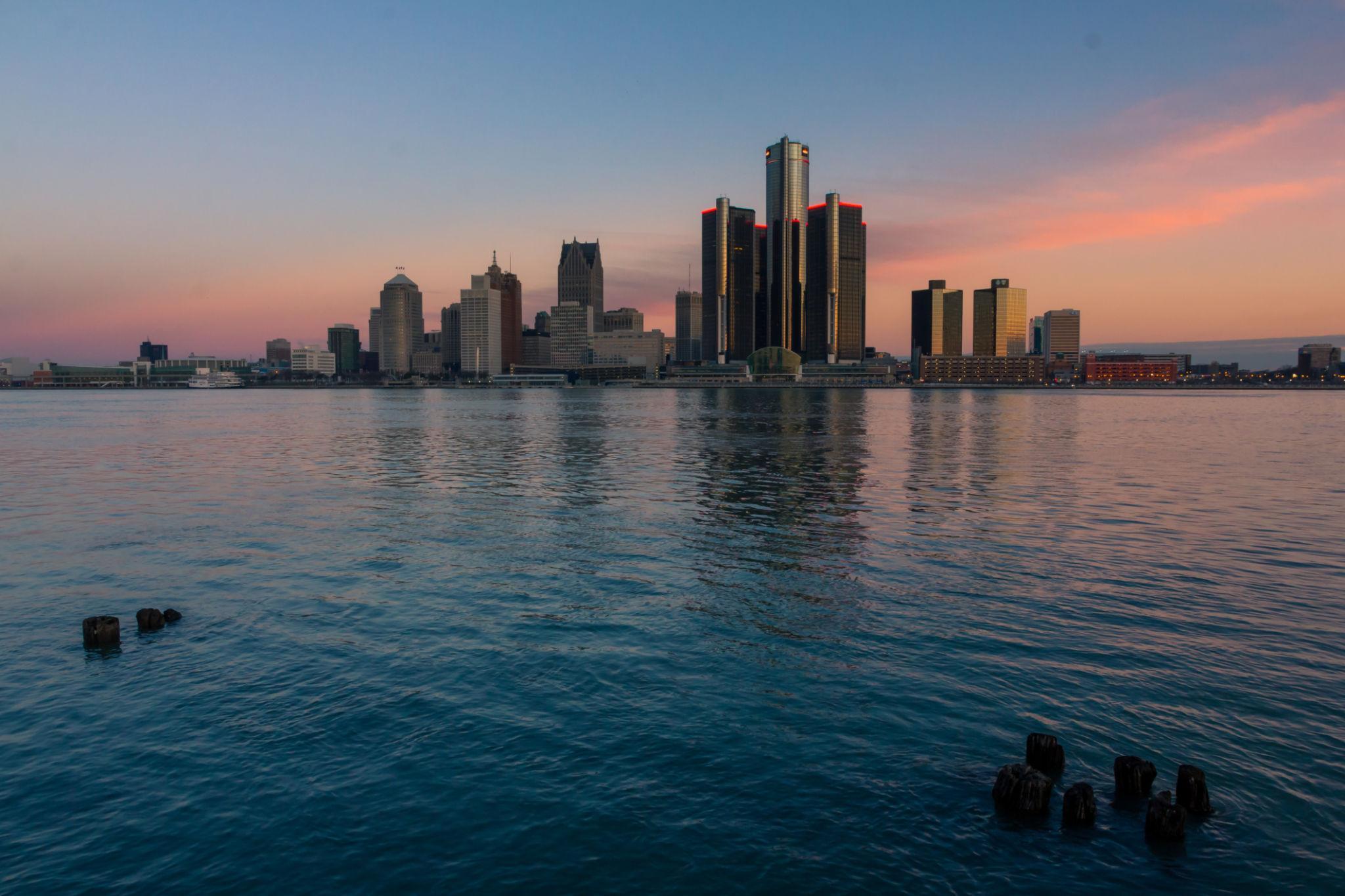 Skyline urbain illuminé au coucher de soleil depuis une baie, avec gratte-ciel reflétés dans l’eau calme