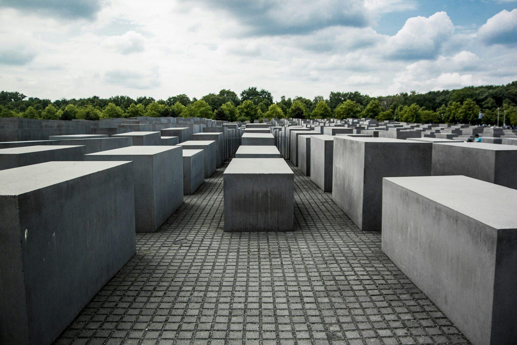 The Holocaust Memorial with its rows of grey concrete stelae under a cloudy sky and a green forest beyond